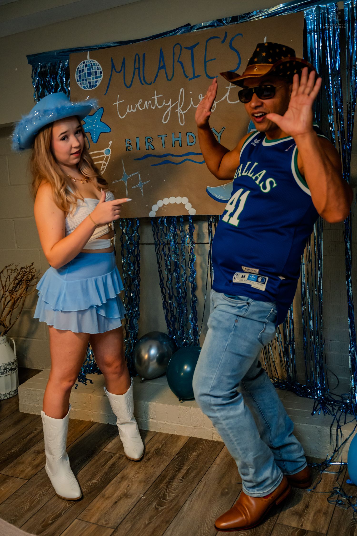 Two guests dance and laugh in front of Malarie's 21st birthday sign with blue party decorations.