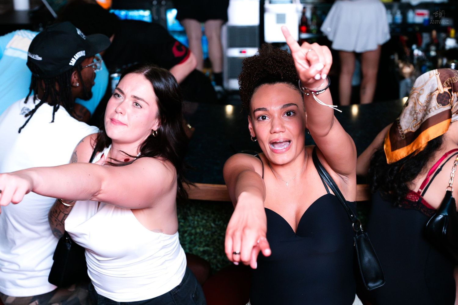 Two women dancing and pointing at the camera at a nightclub party.