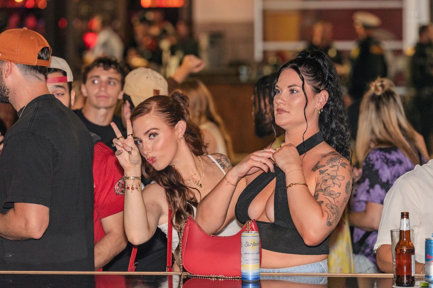 Two women leaning on a bar railing watching a performance at a busy nightlife venue.