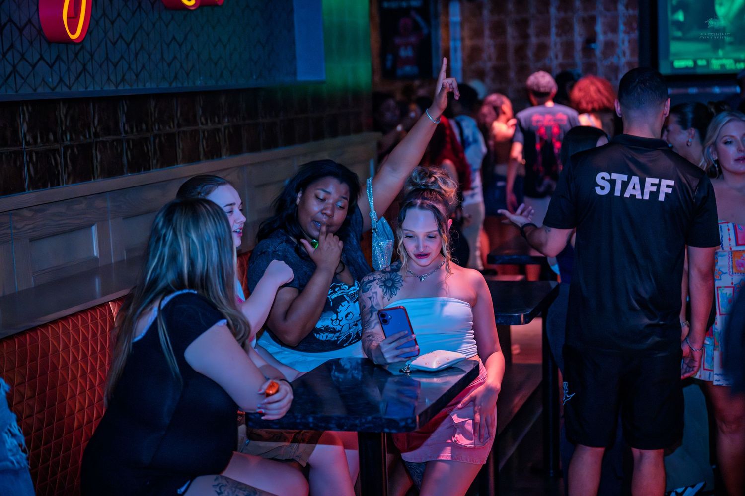 Women looking at a tablet at a busy nightclub with staff member nearby.