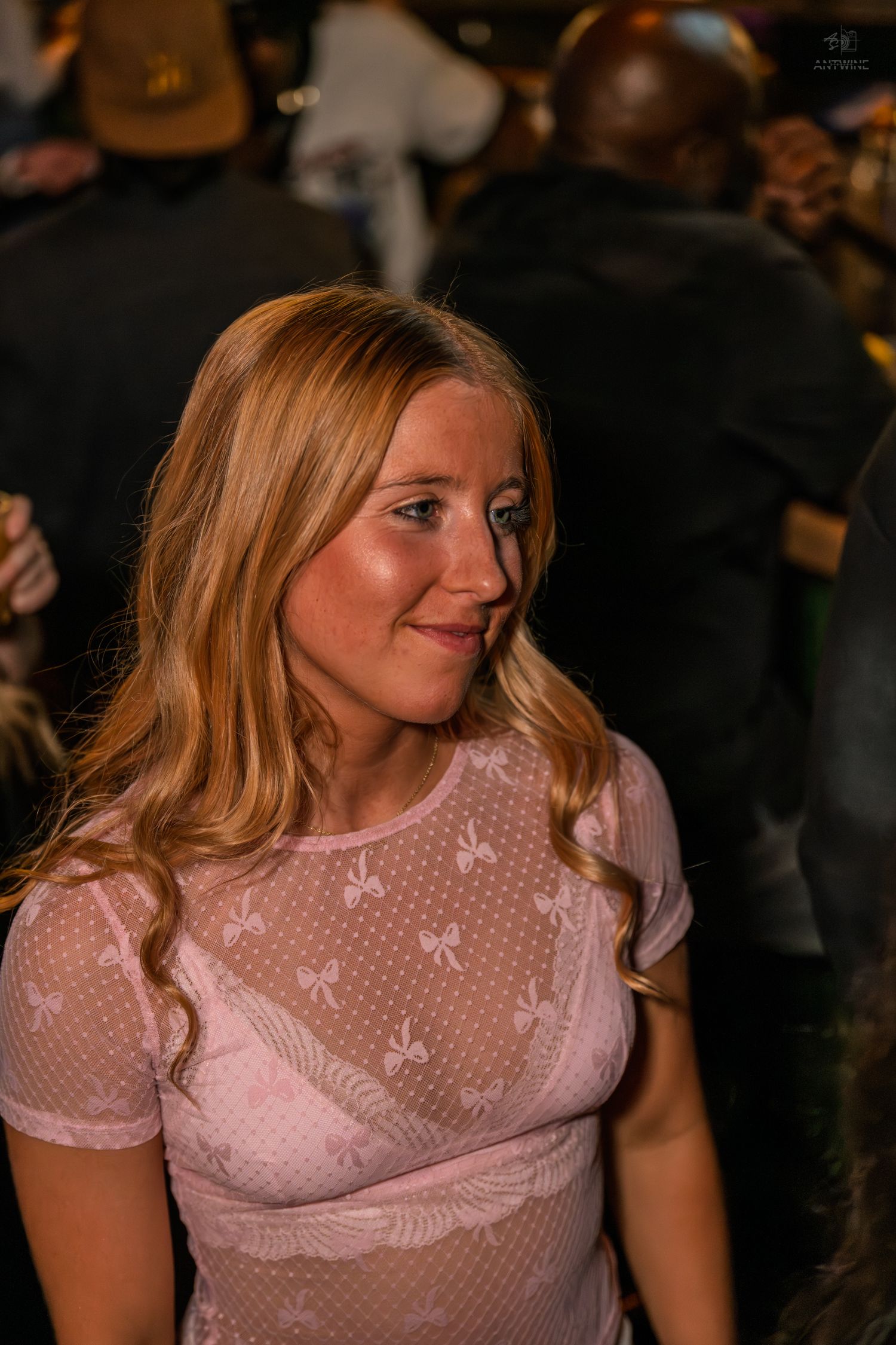 Smiling blonde woman in pink sheer top at a nightlife event.