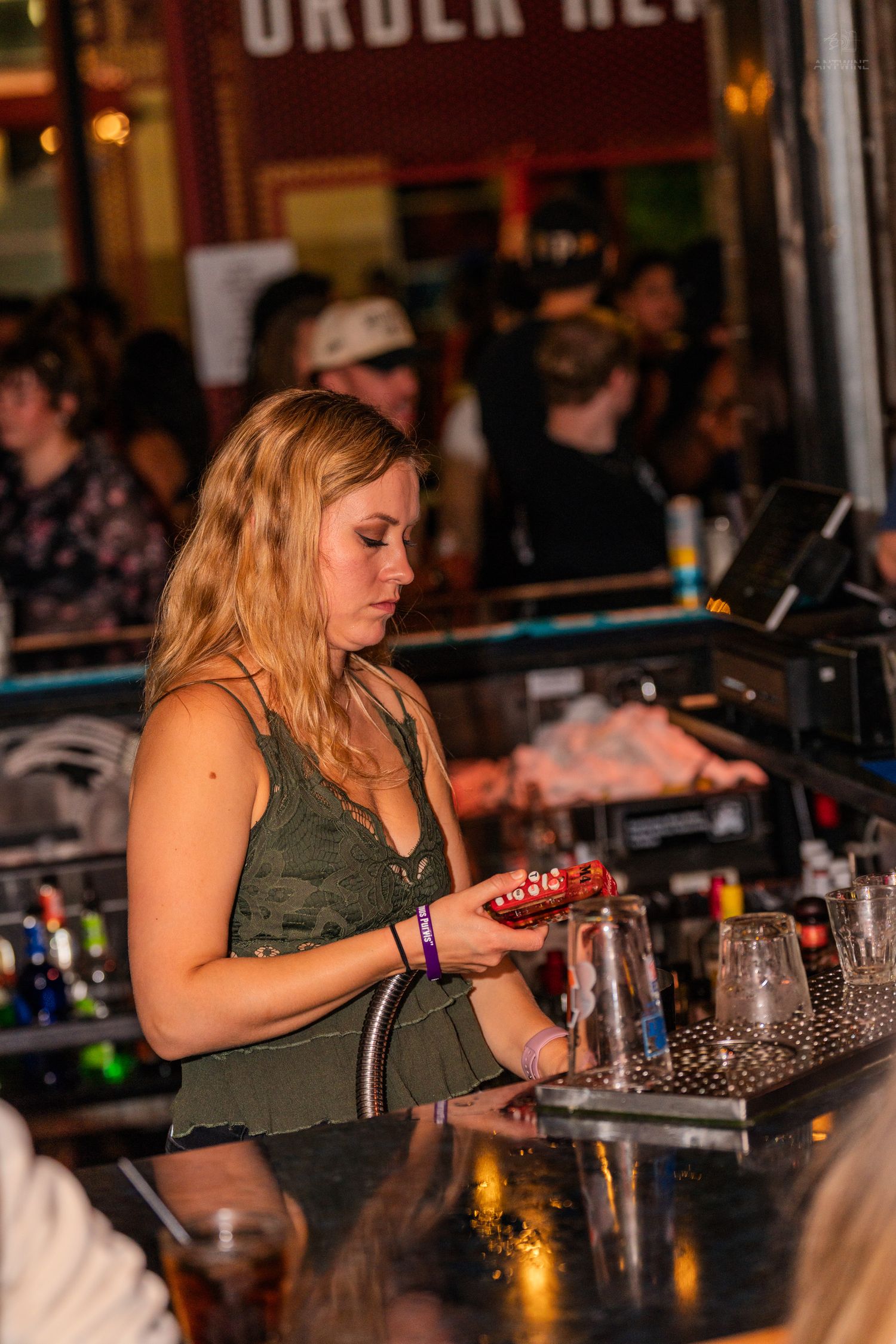 Female bartender preparing drinks at a busy bar counter.