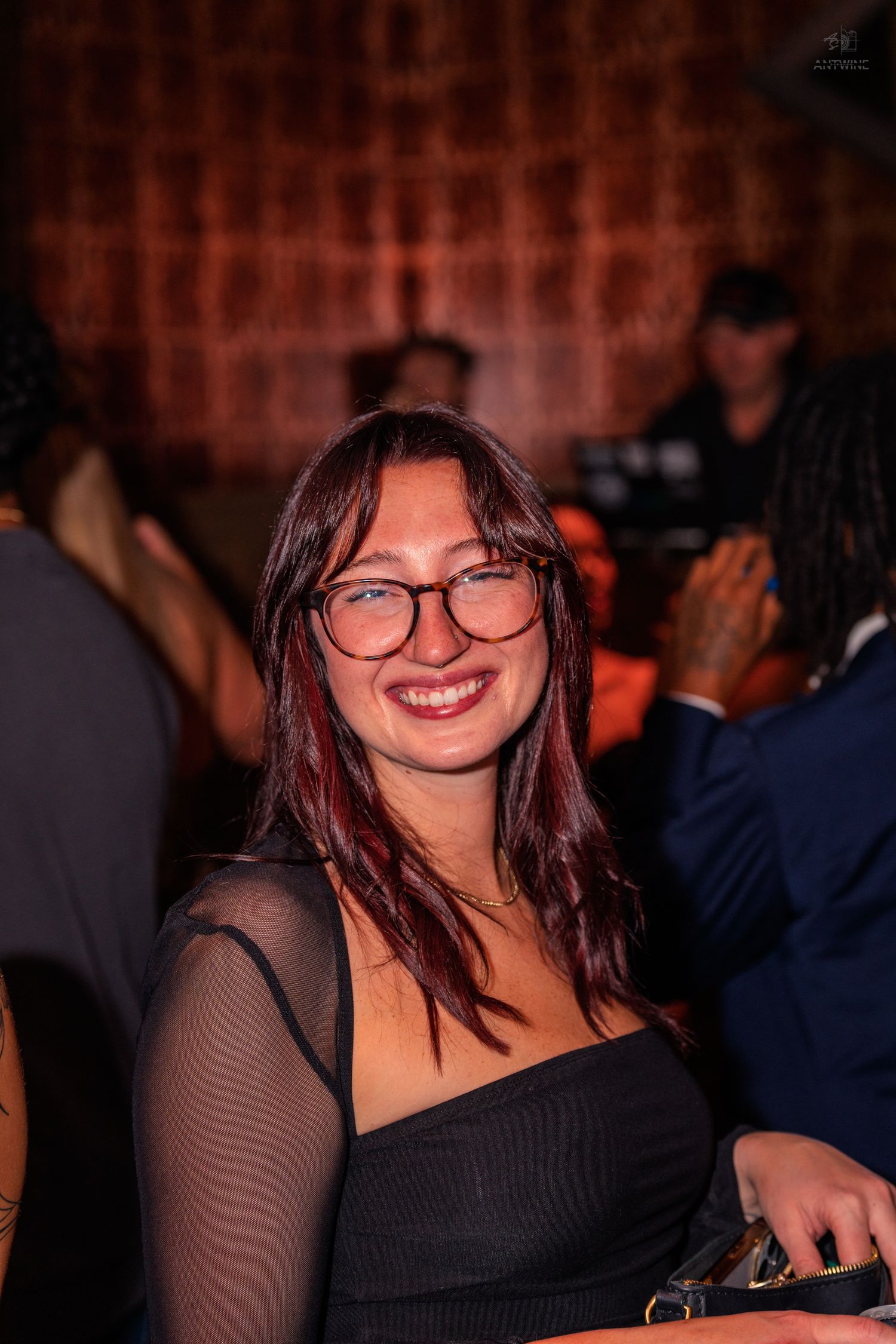 Smiling young woman with glasses and dark red hair at a nightclub event.