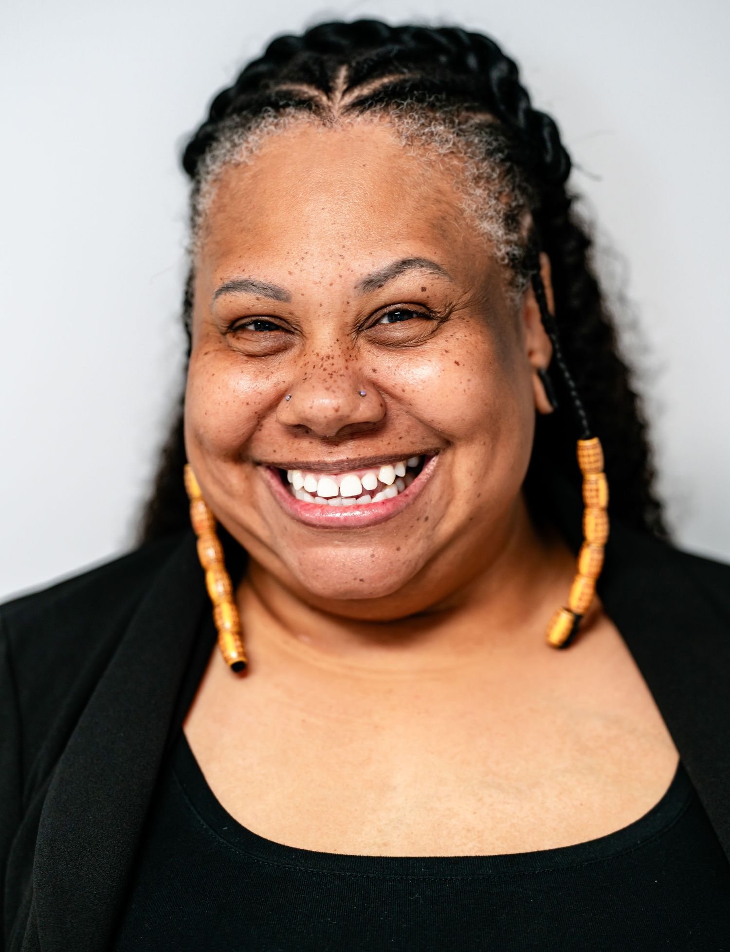 Laughing Black woman with braided hair and yellow beaded earrings wearing black outfit, close-up portrait.