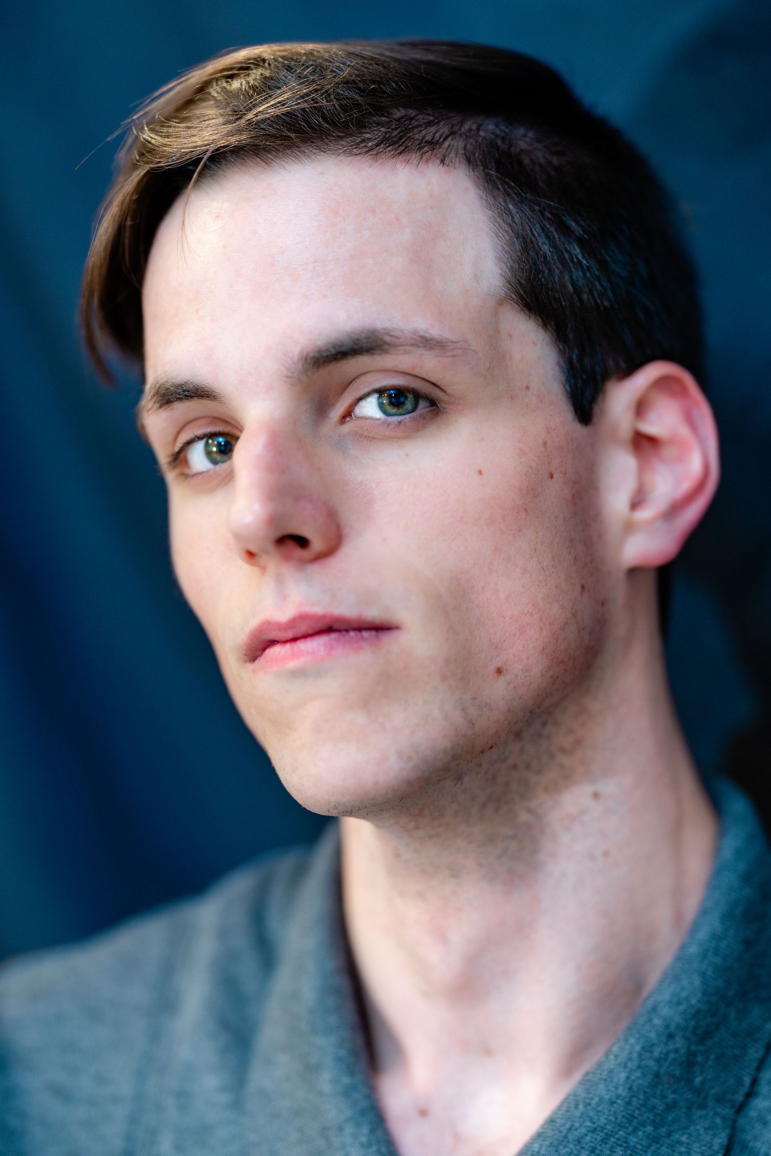 Close-up portrait of young man with light eyes and short brown hair wearing gray shirt.