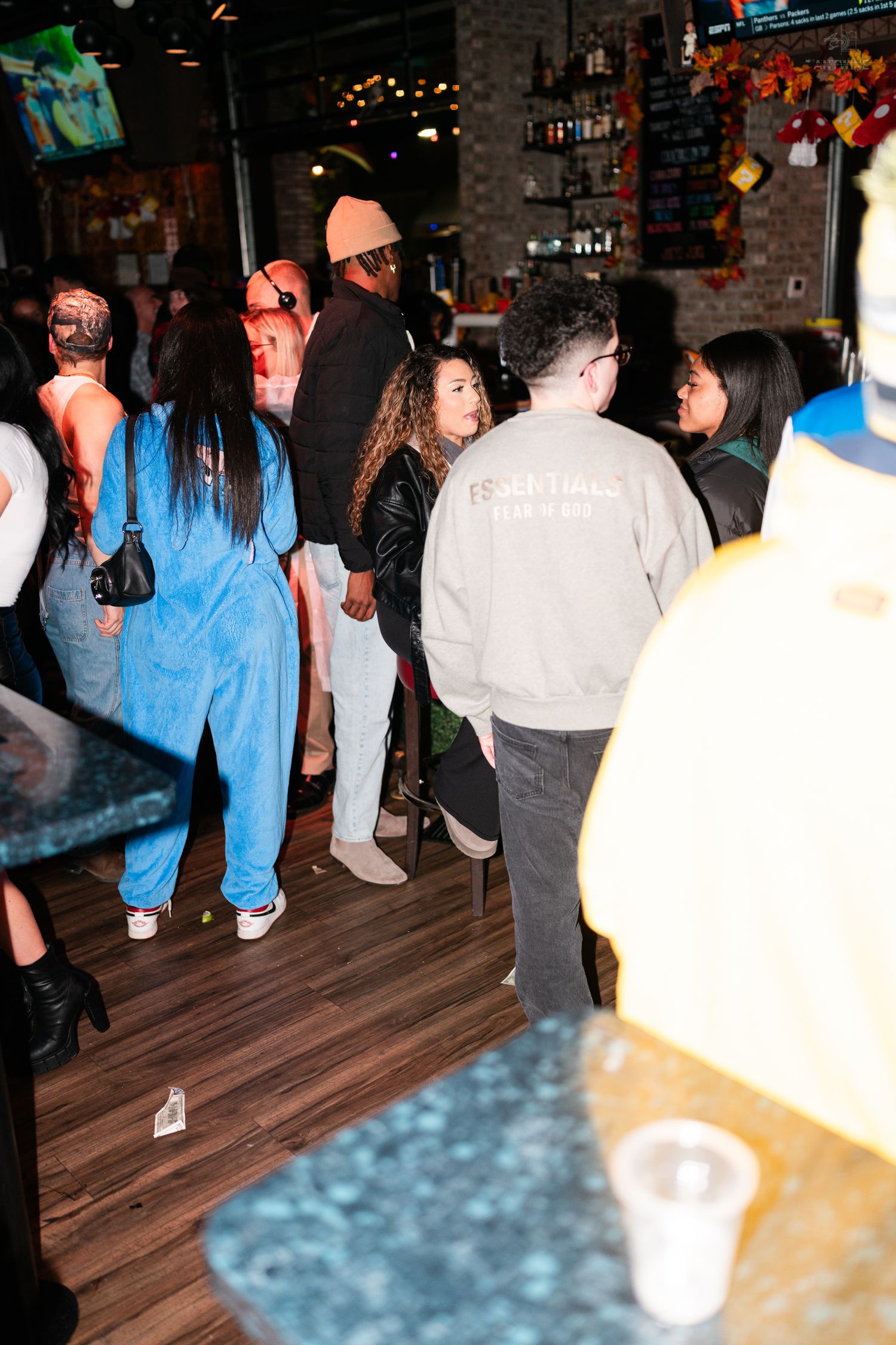 Diverse group of people in Halloween costumes mingling inside a busy bar and nightclub venue.