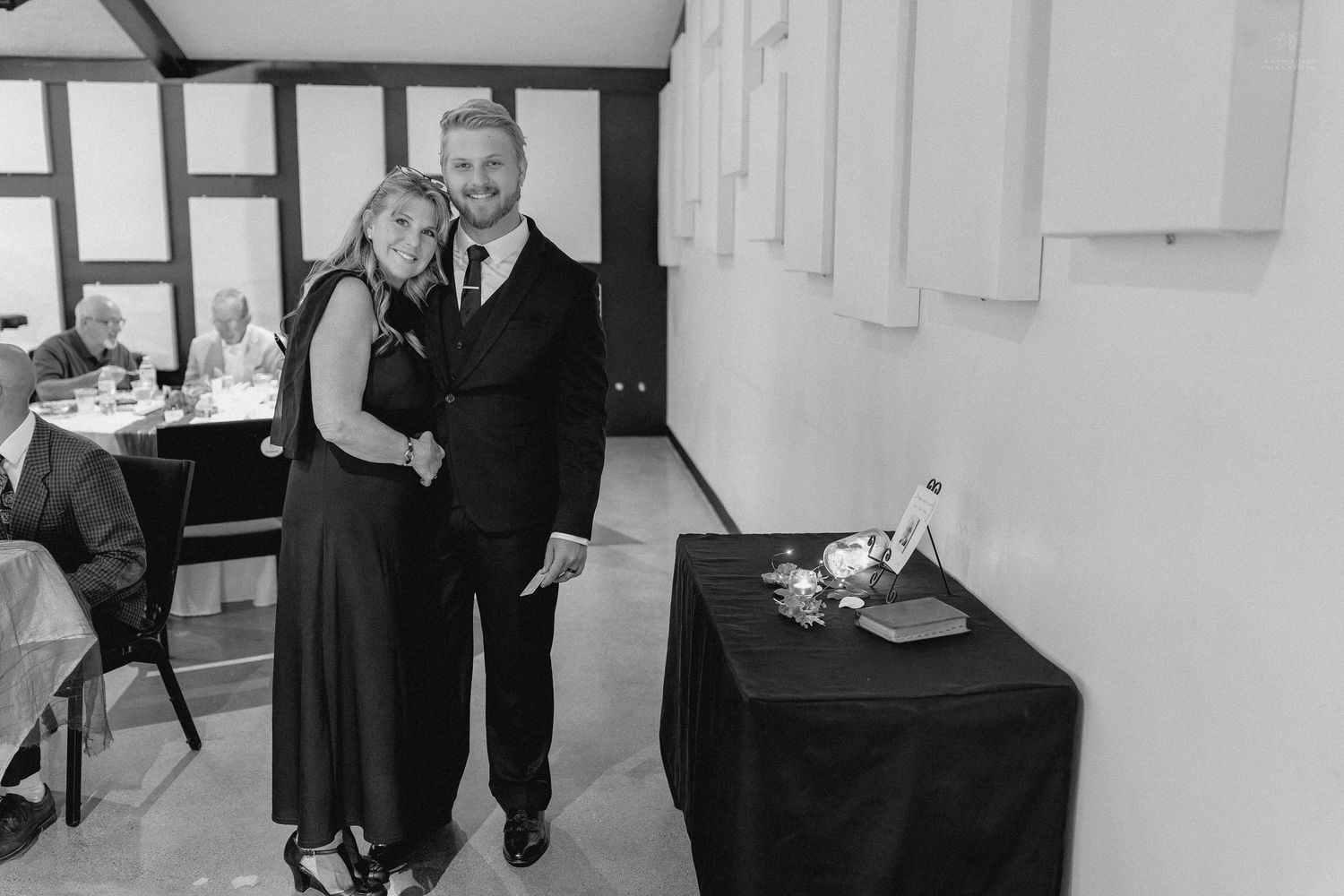 Black and white photo of a smiling couple posing together near a decorated table at a wedding reception.