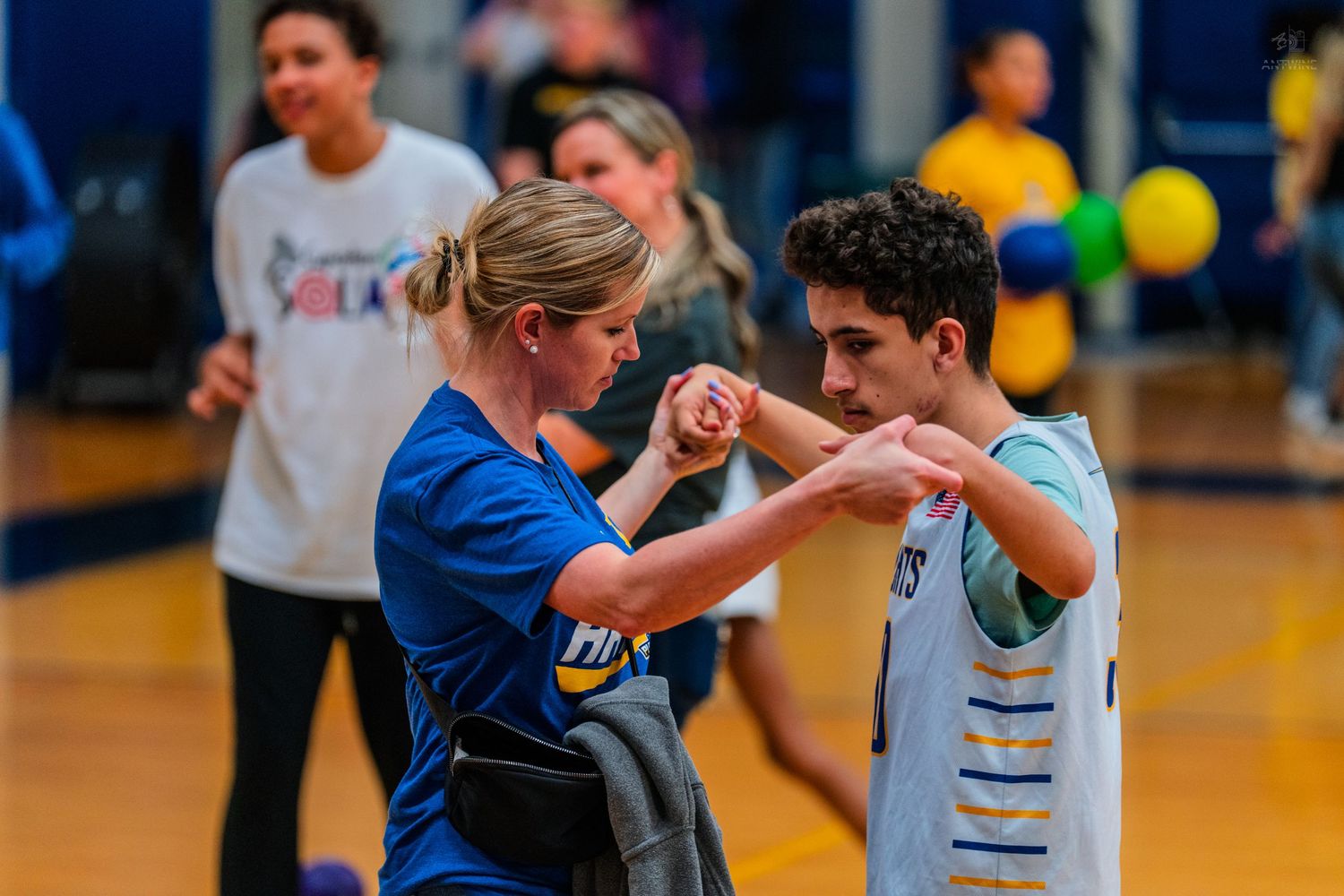 A woman in blue shirt fist-bumping a teenage boy during an indoor gymnasium sports activity.