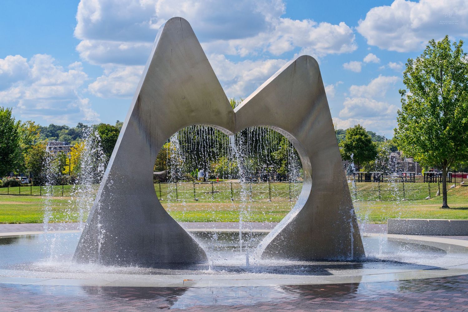 Abstract concrete fountain sculpture with water jets in a sunny park setting with blue skies.