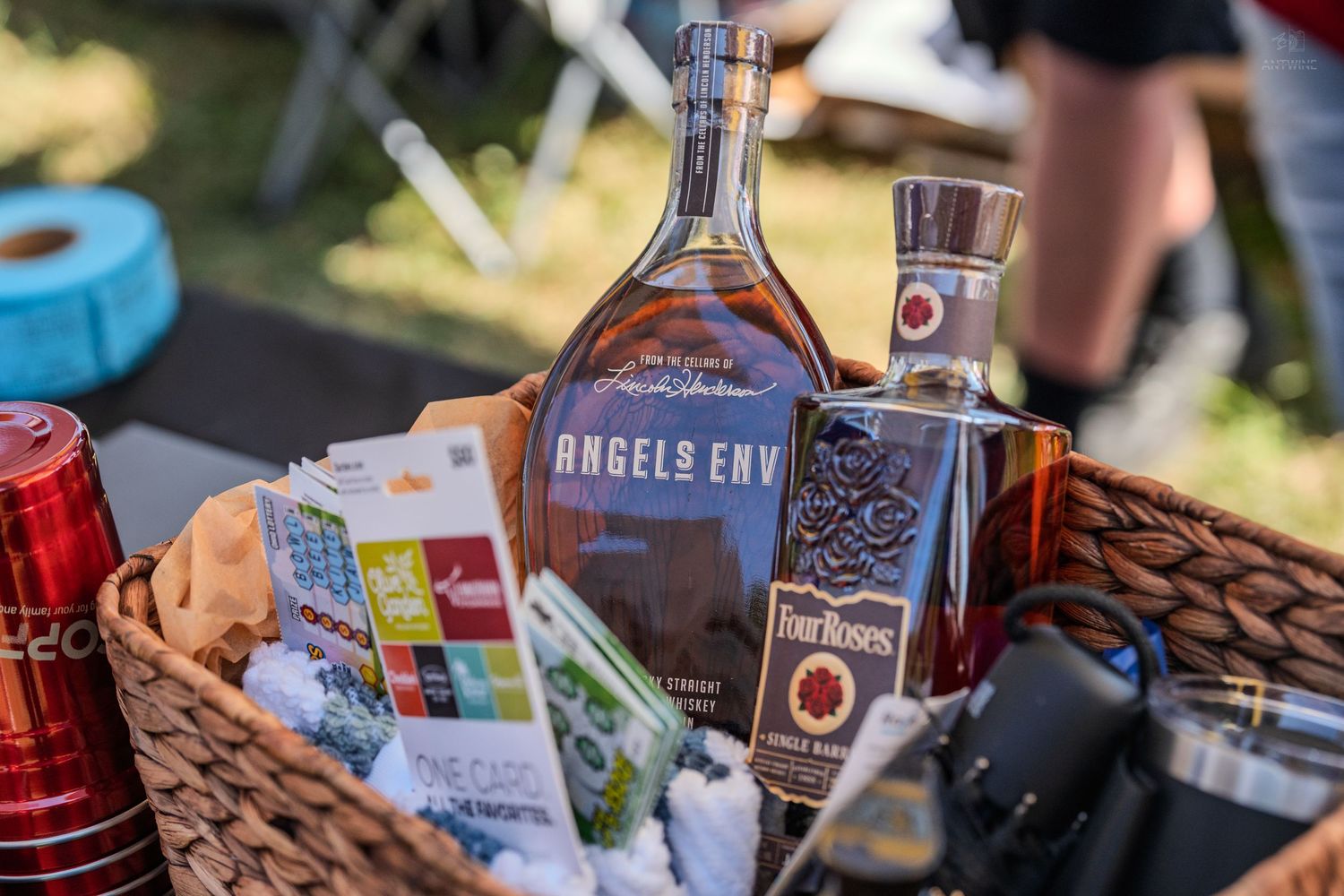 Gift basket containing Angels Envy and Four Roses bourbon whiskey bottles at outdoor event.