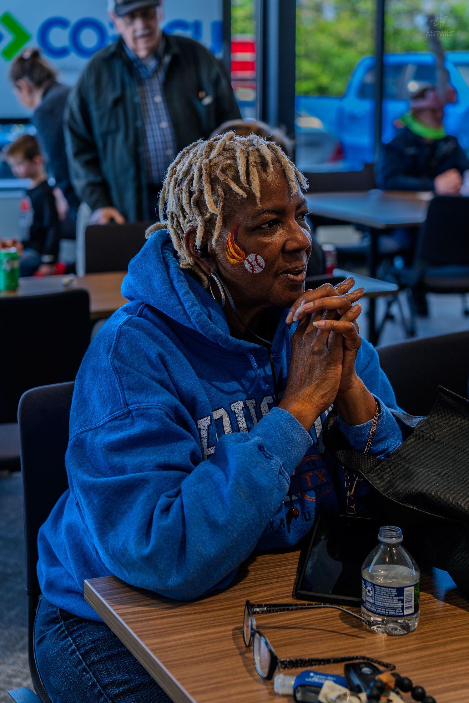 Woman in blue hoodie sits at table with clasped hands at a COPECU community event.