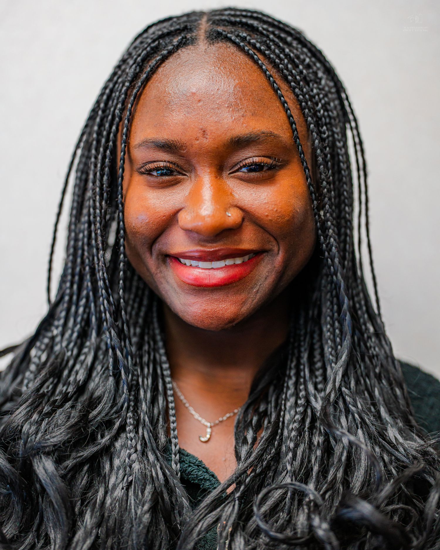 Smiling young Black woman with long box braids, wearing red lipstick and a delicate necklace, posing for a portrait.