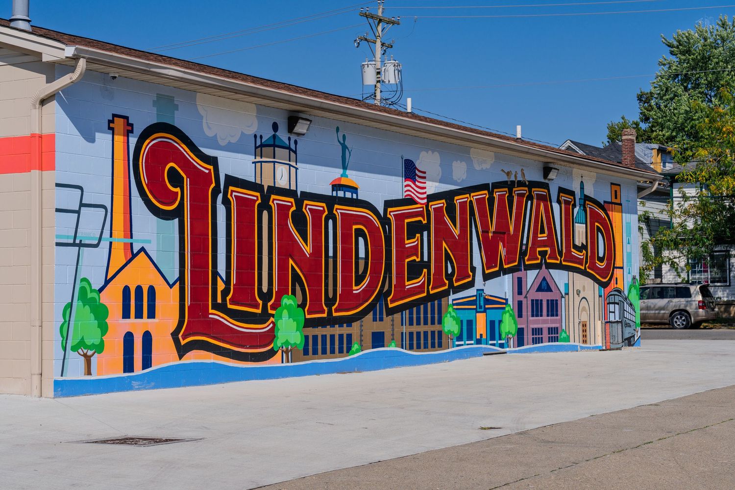 Colorful Lindenwald neighborhood mural on building exterior featuring bold lettering, factories, and trees.