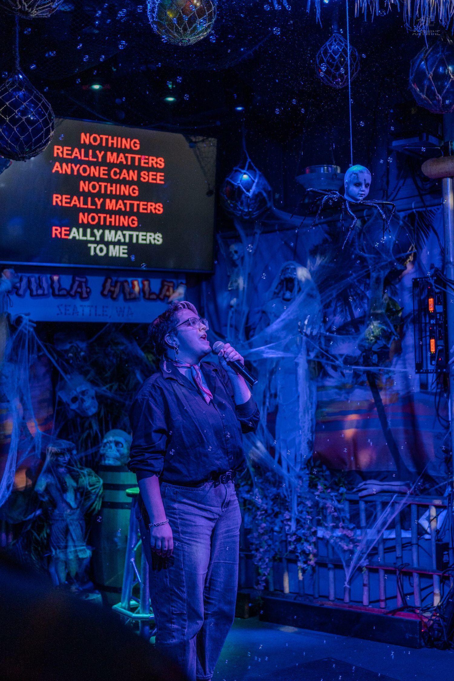 Singer performing karaoke in a spooky Halloween-themed bar with blue lighting and skull decor.