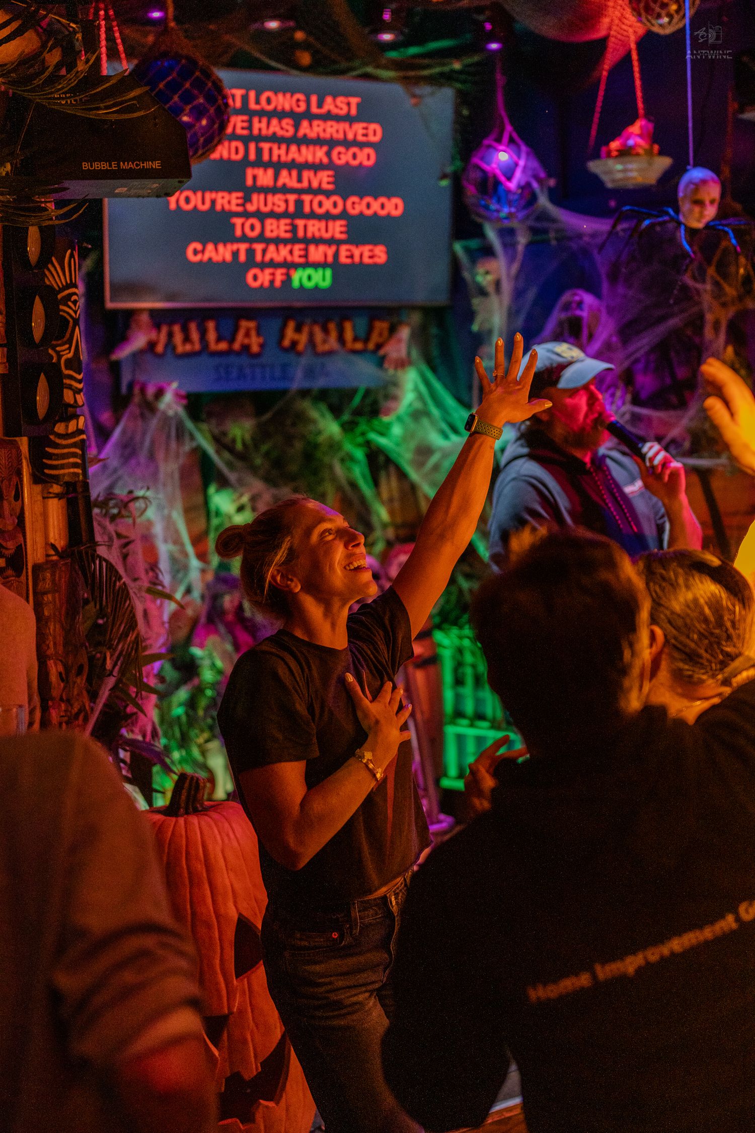 Person singing karaoke at Hula Hula Seattle bar with Halloween decorations and colorful neon lights.