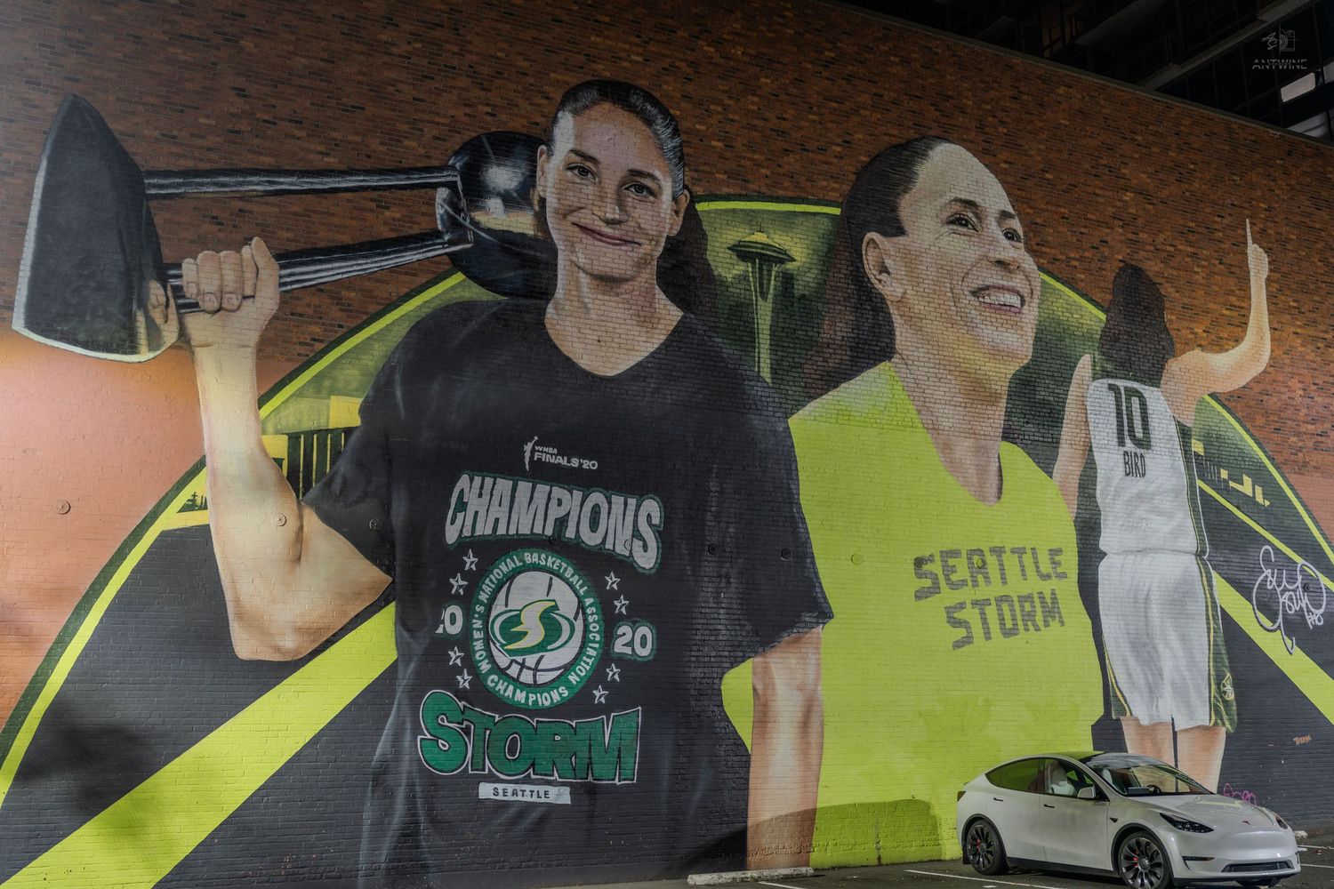 Seattle Storm WNBA Champions 2020 mural featuring two players, one holding a sledgehammer, painted on a building wall.