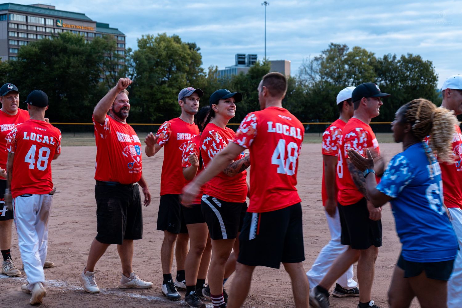 softball team in red Local 48 uniforms celebrating on field after game.