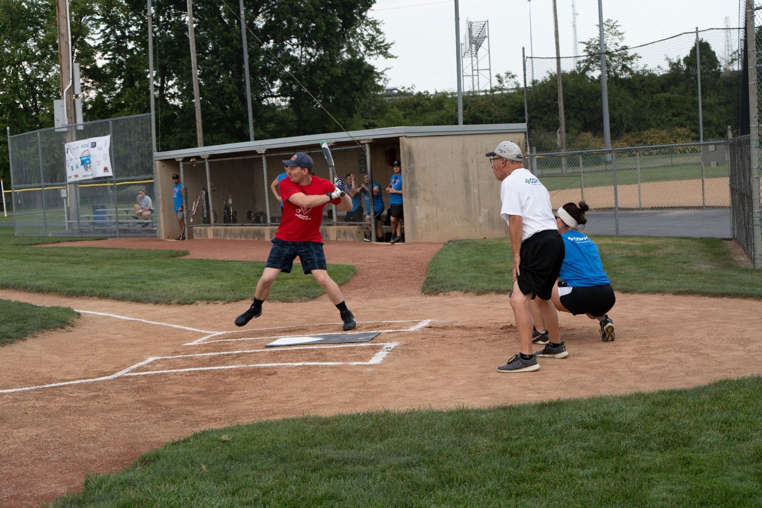 People playing softball at a baseball diamond, with a batter in red shirt and two other players near home plate.