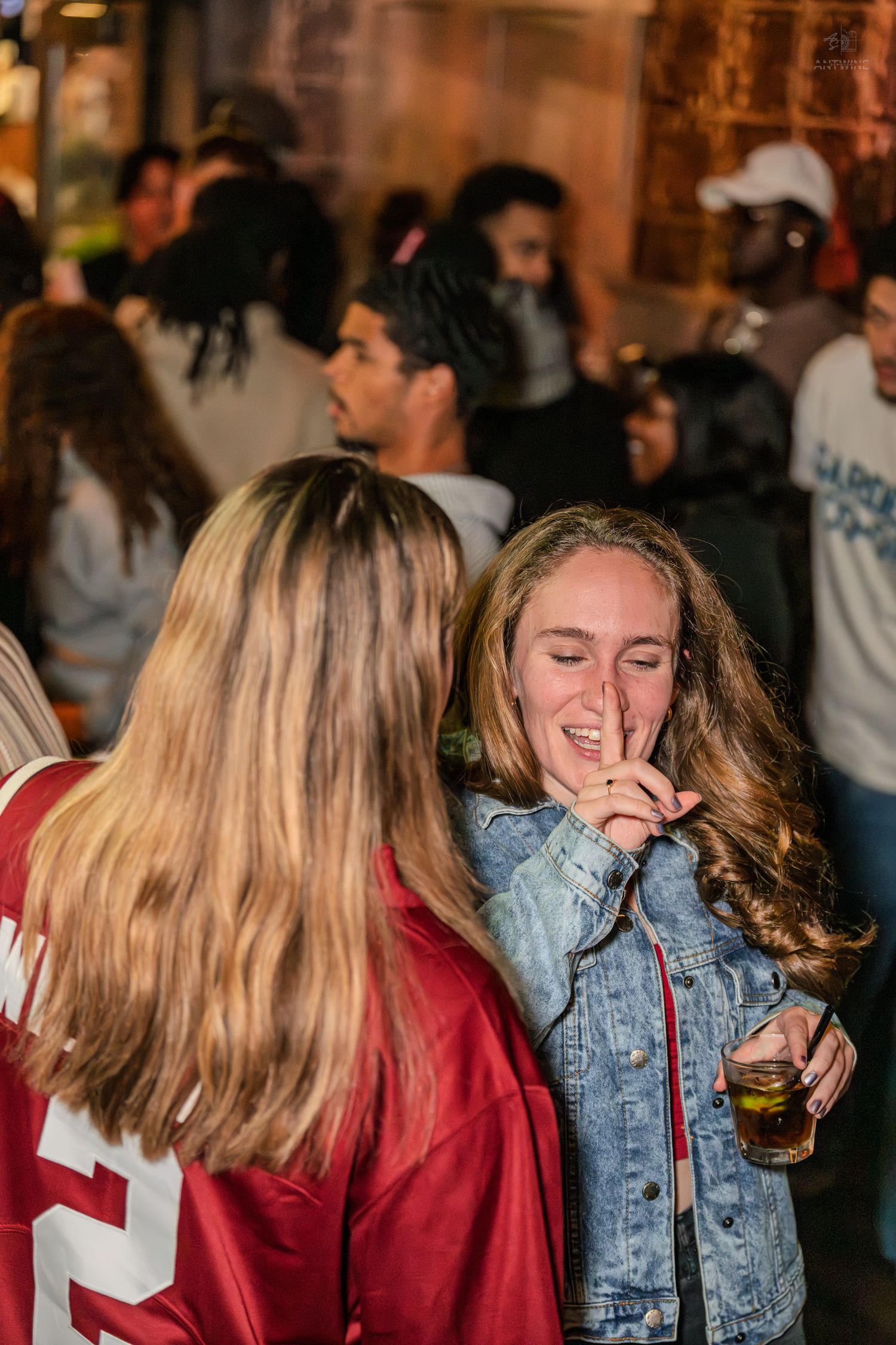 Two women laughing together at an outdoor nightlife event holding drinks.