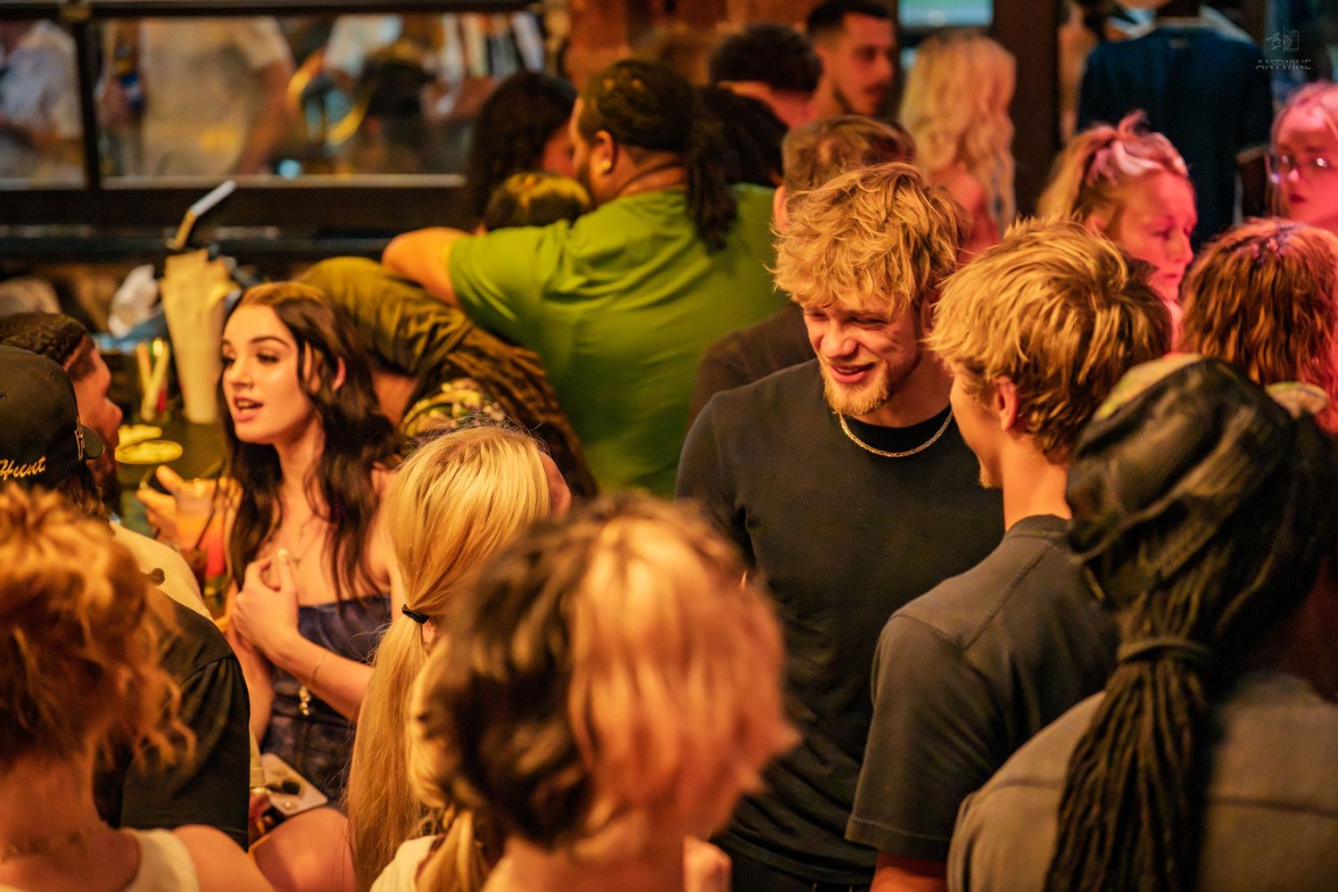 Group of young people socializing in a crowded warmly lit indoor venue.