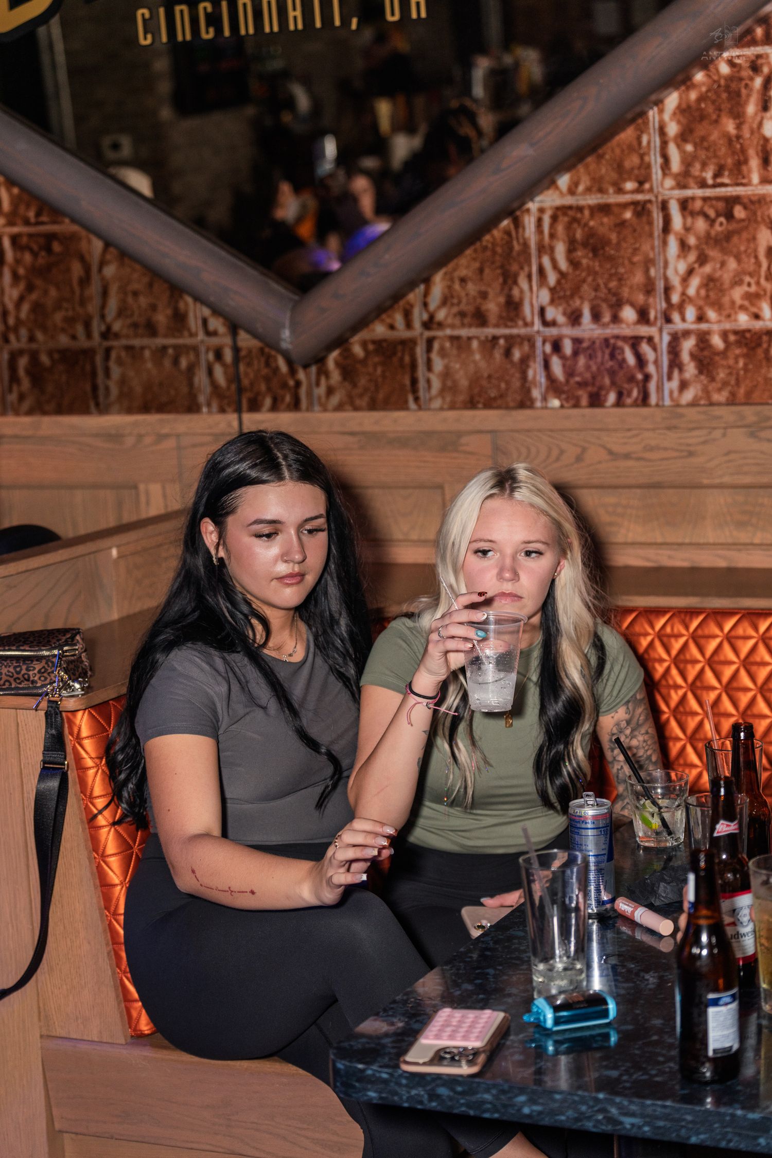 Two young women sitting in a booth at a Cincinnati bar enjoying drinks together.