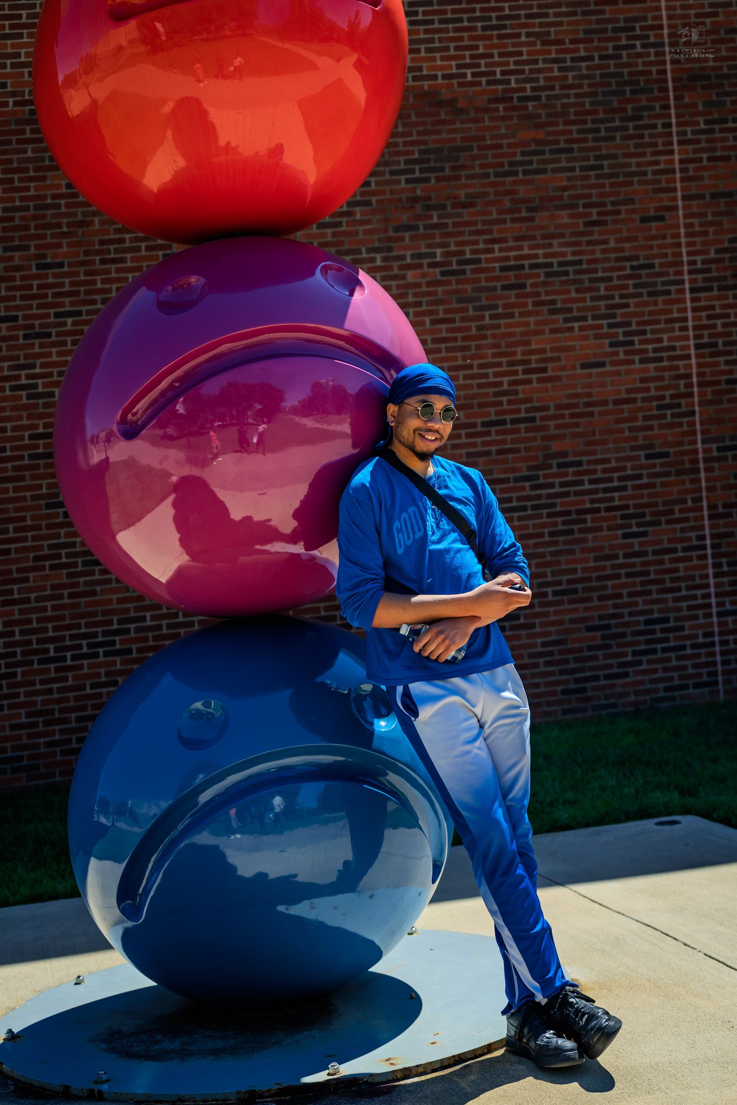 Smiling man in blue outfit posing beside vibrant red, purple, and blue spherical art sculpture.
