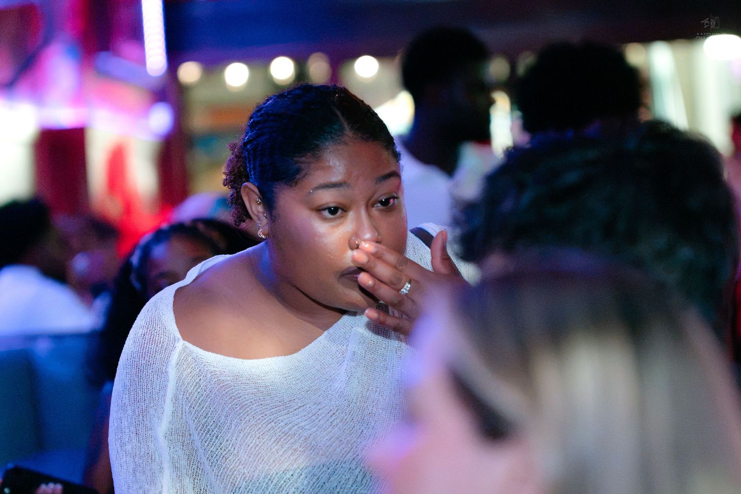 Young woman covering her mouth with hand at a vibrant nightclub social gathering.