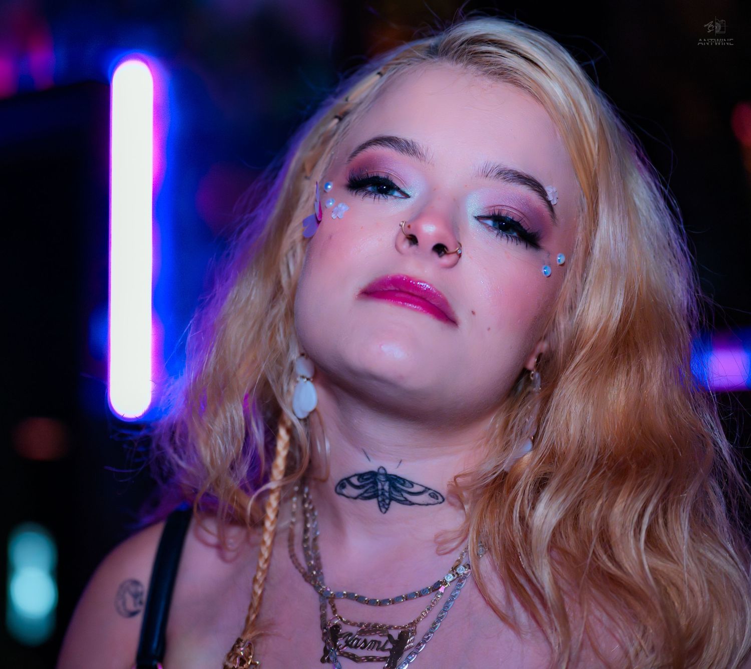 Close-up portrait of tattooed blonde woman with glitter makeup and neon lights.