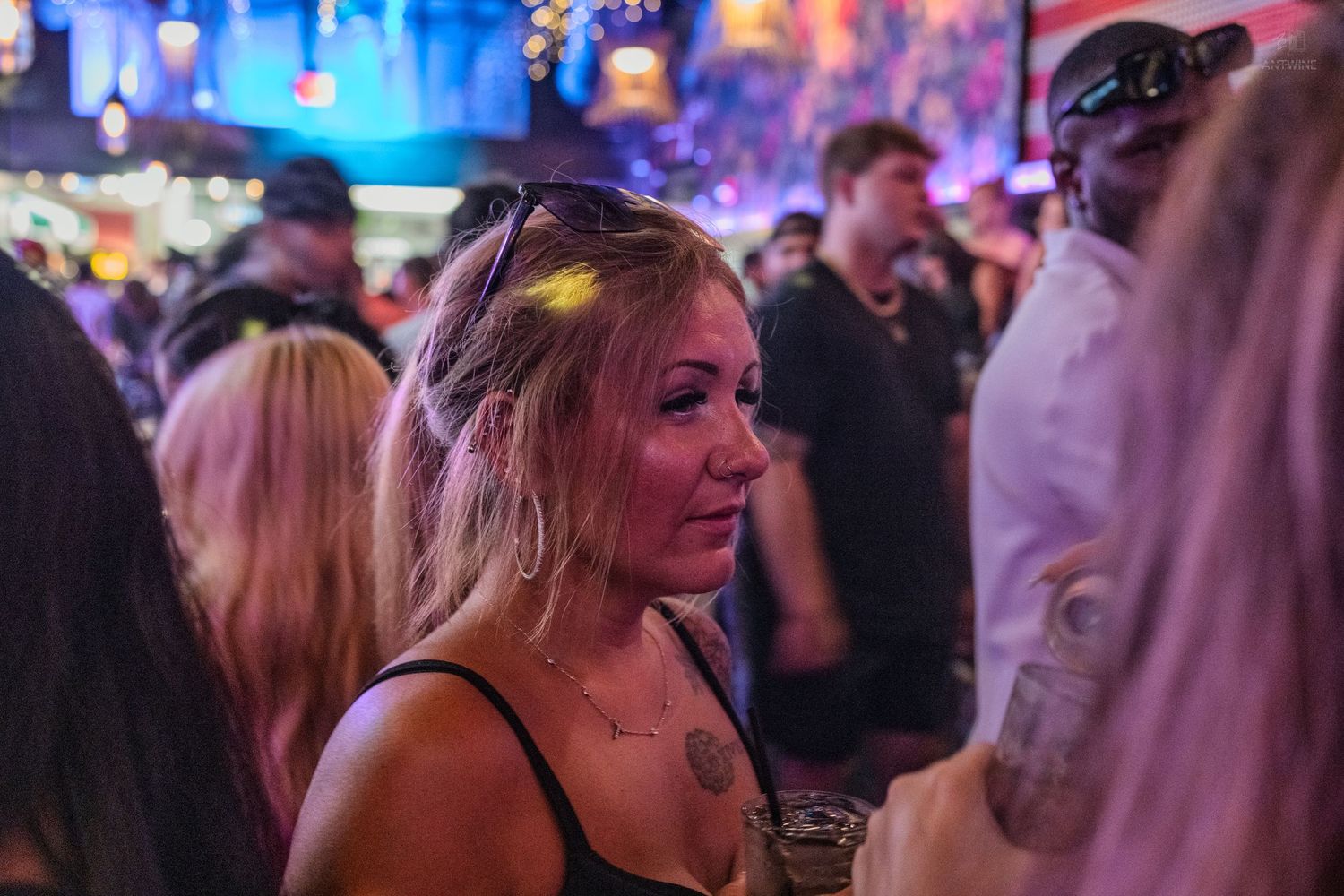 Tattooed blonde woman in a crowded colorful nightclub setting.
