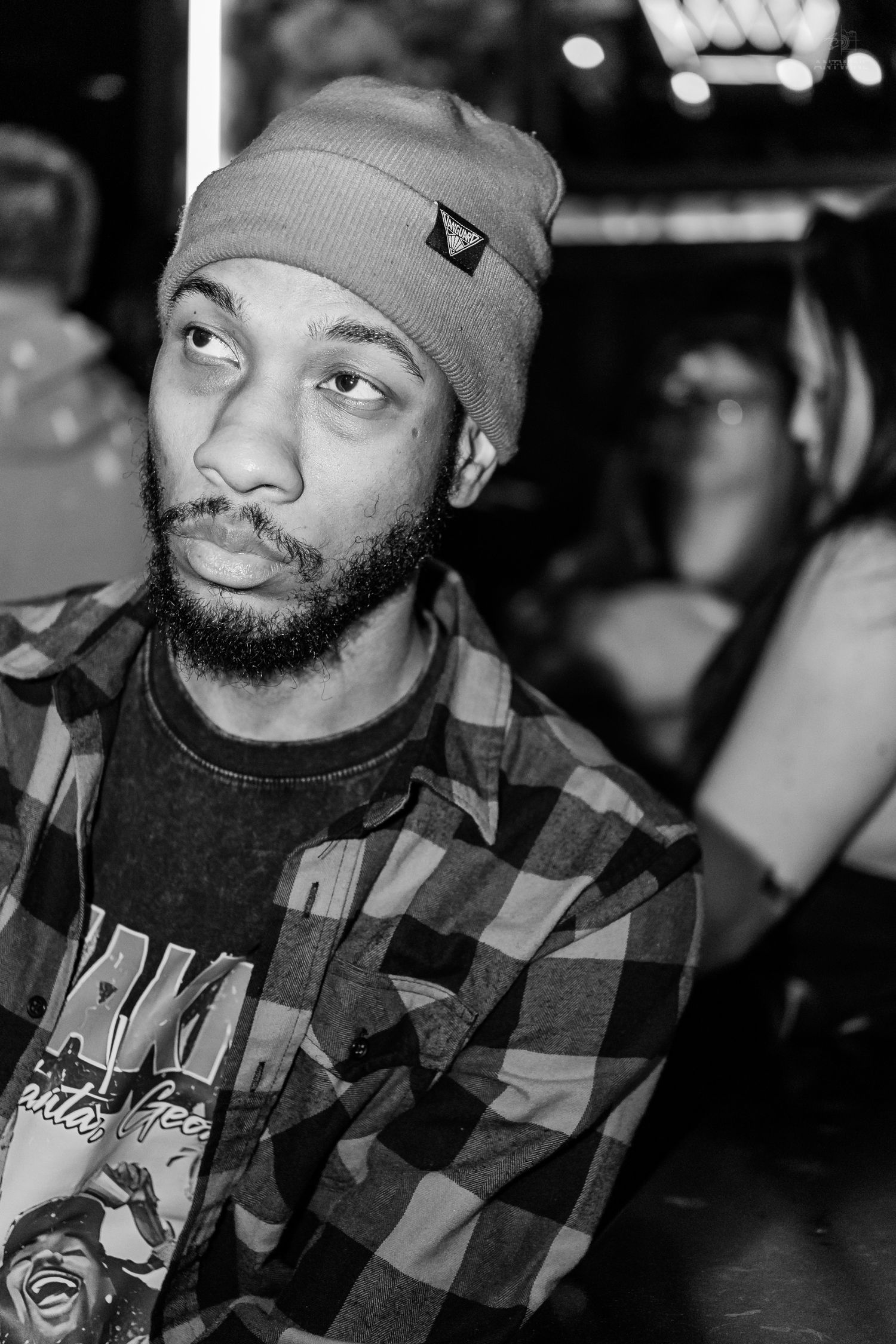 Close-up portrait of bearded man in beanie and plaid shirt at a nightclub event.