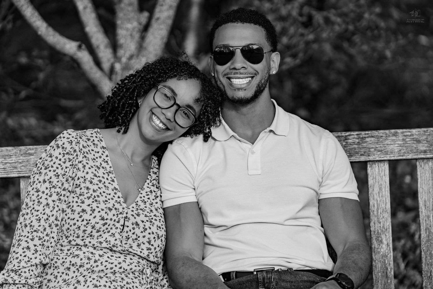 Black and white photo of a happy couple sitting on a bench, woman resting head on mans shoulder.