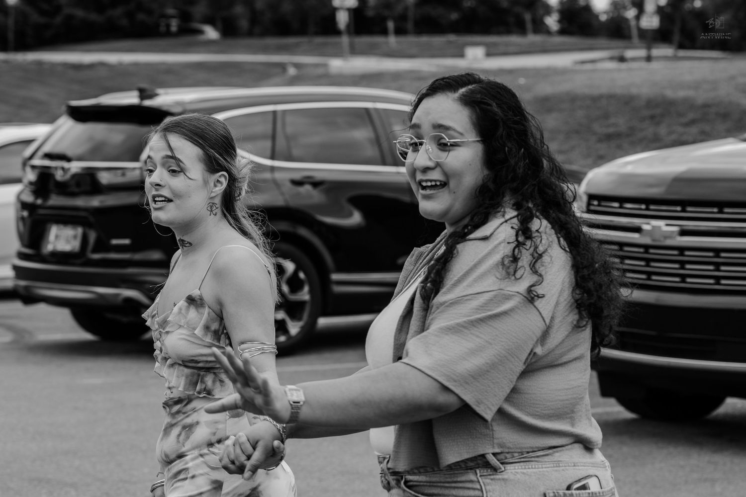 Two young women laugh and dance together in a parking lot in this fun black and white photo.