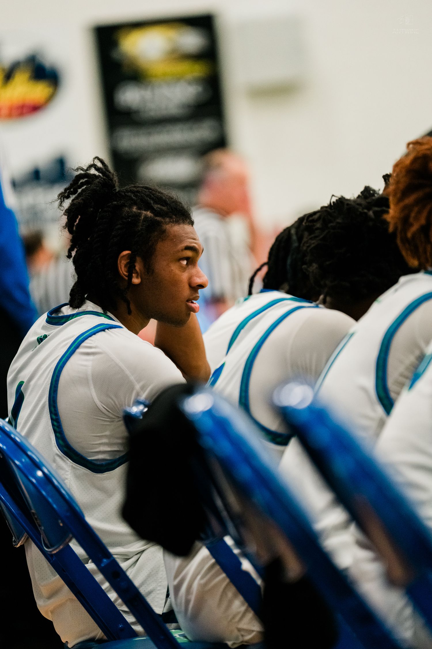 Basketball player with braided hair sits on bench during a game.