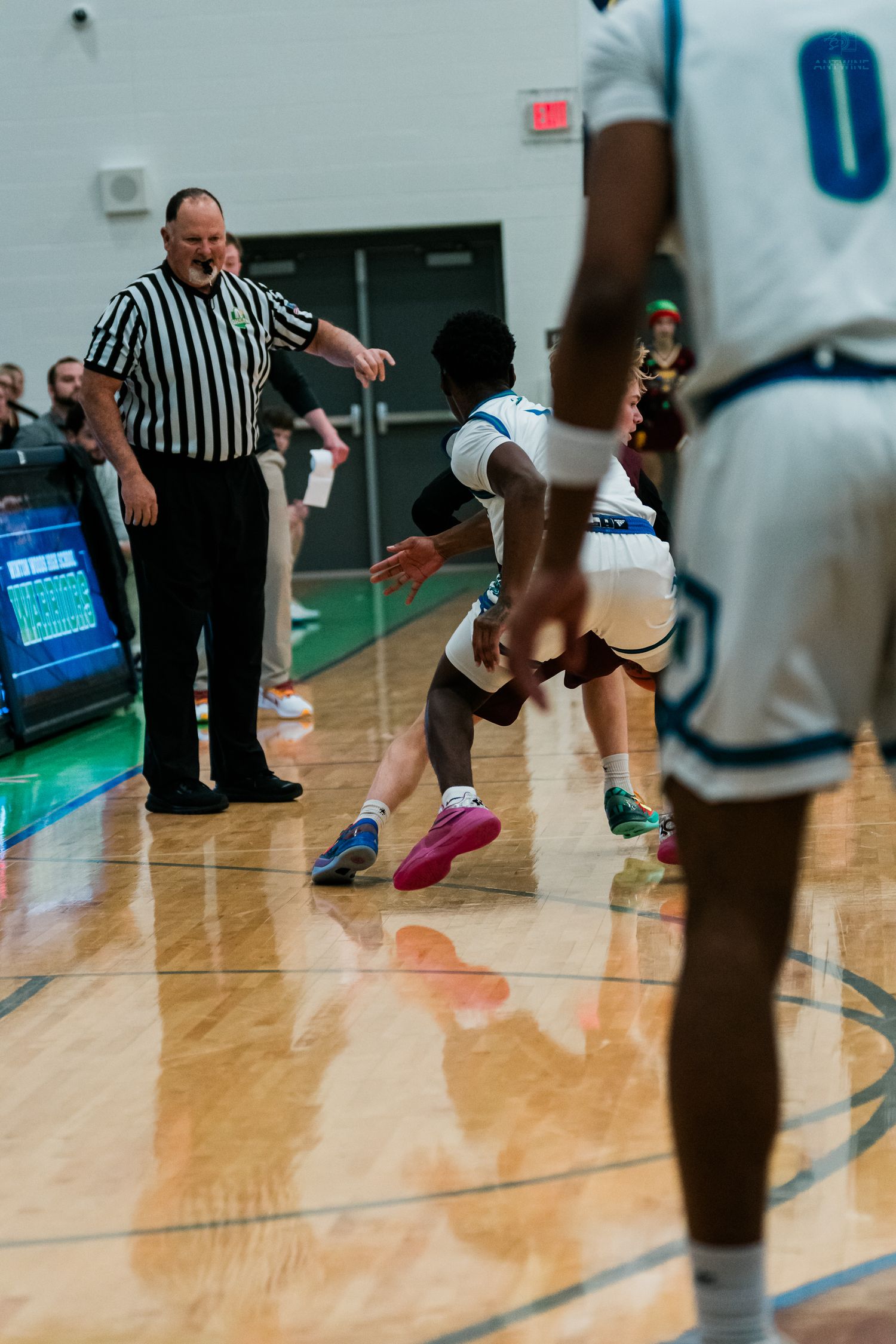 Referee signals call as Warriors player dribbles during high school basketball game on court.