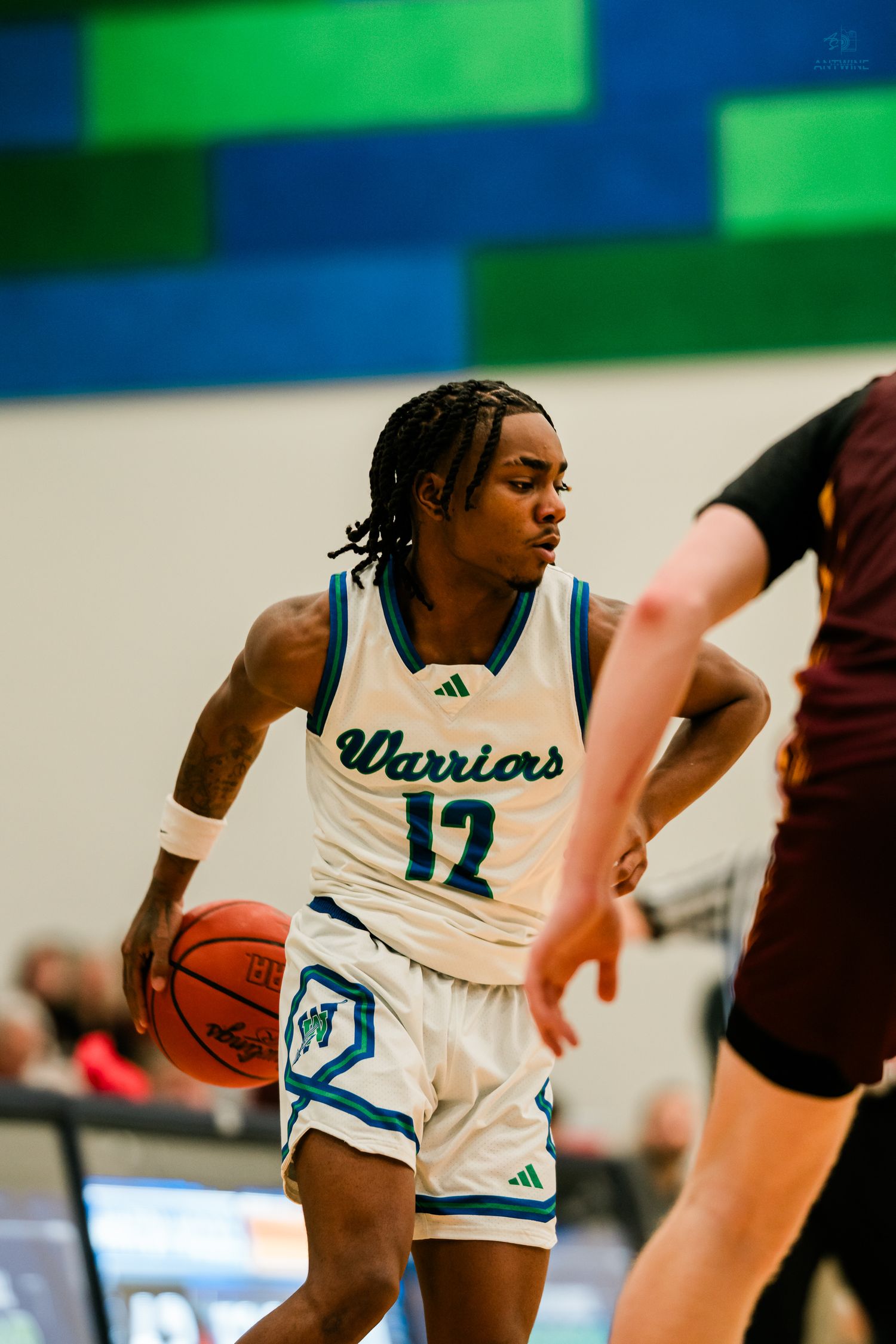 Warriors player number 12 dribbles the ball while driving past a maroon-jersey defender on the court.