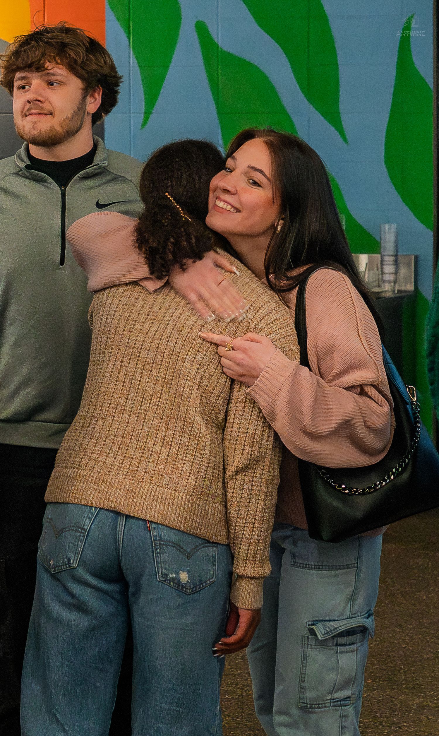 Two young women sharing a warm hug at a casual social gathering inside a brewery.