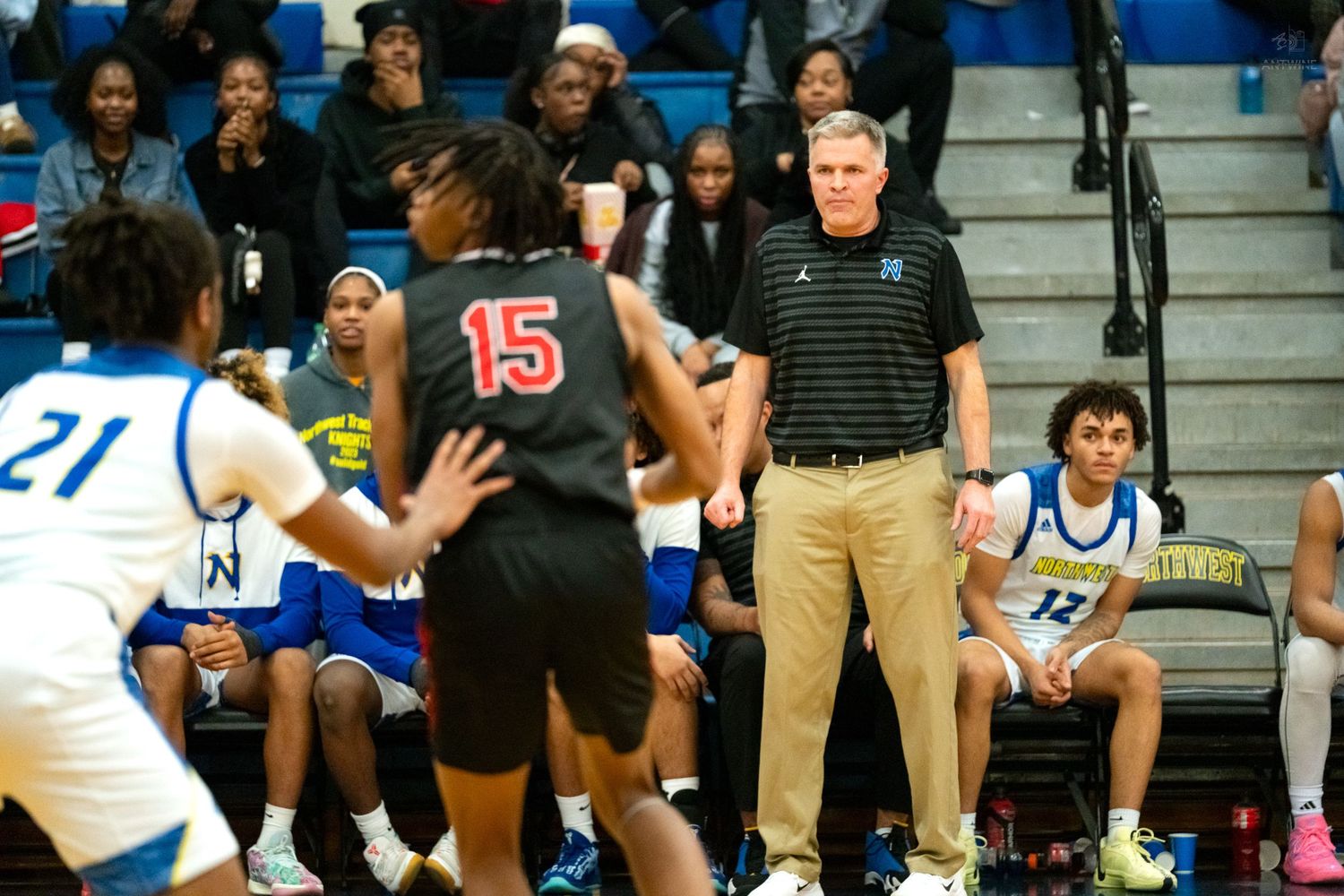 Coach watches player #15 in black uniform during competitive high school basketball game.