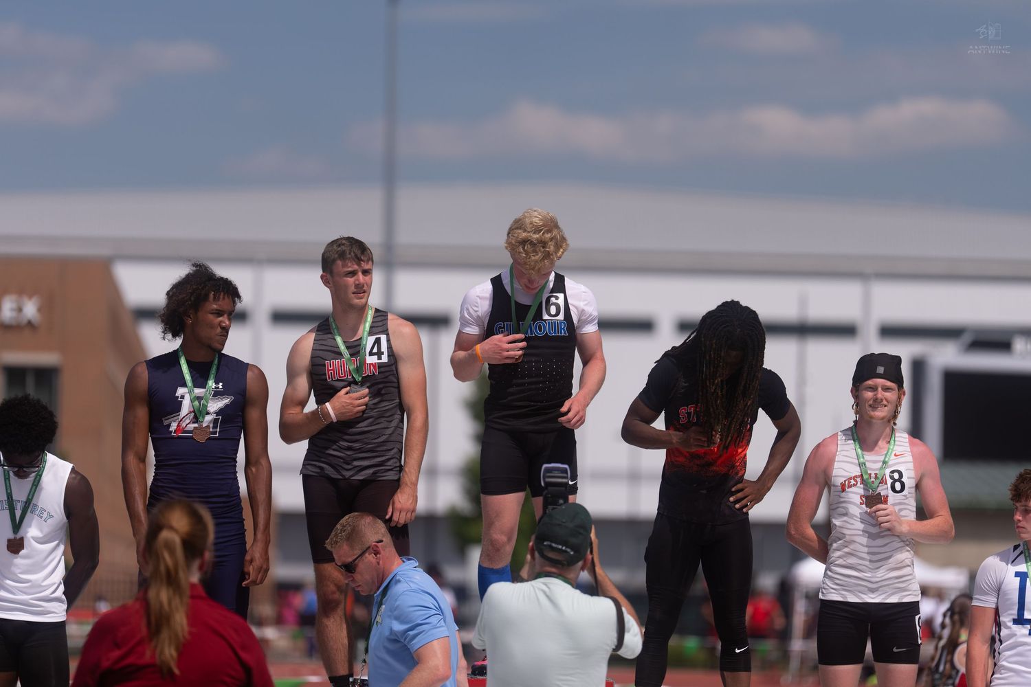 Young athletes stand on a track podium at an OHSAA boys track meet awaiting medal ceremony results.