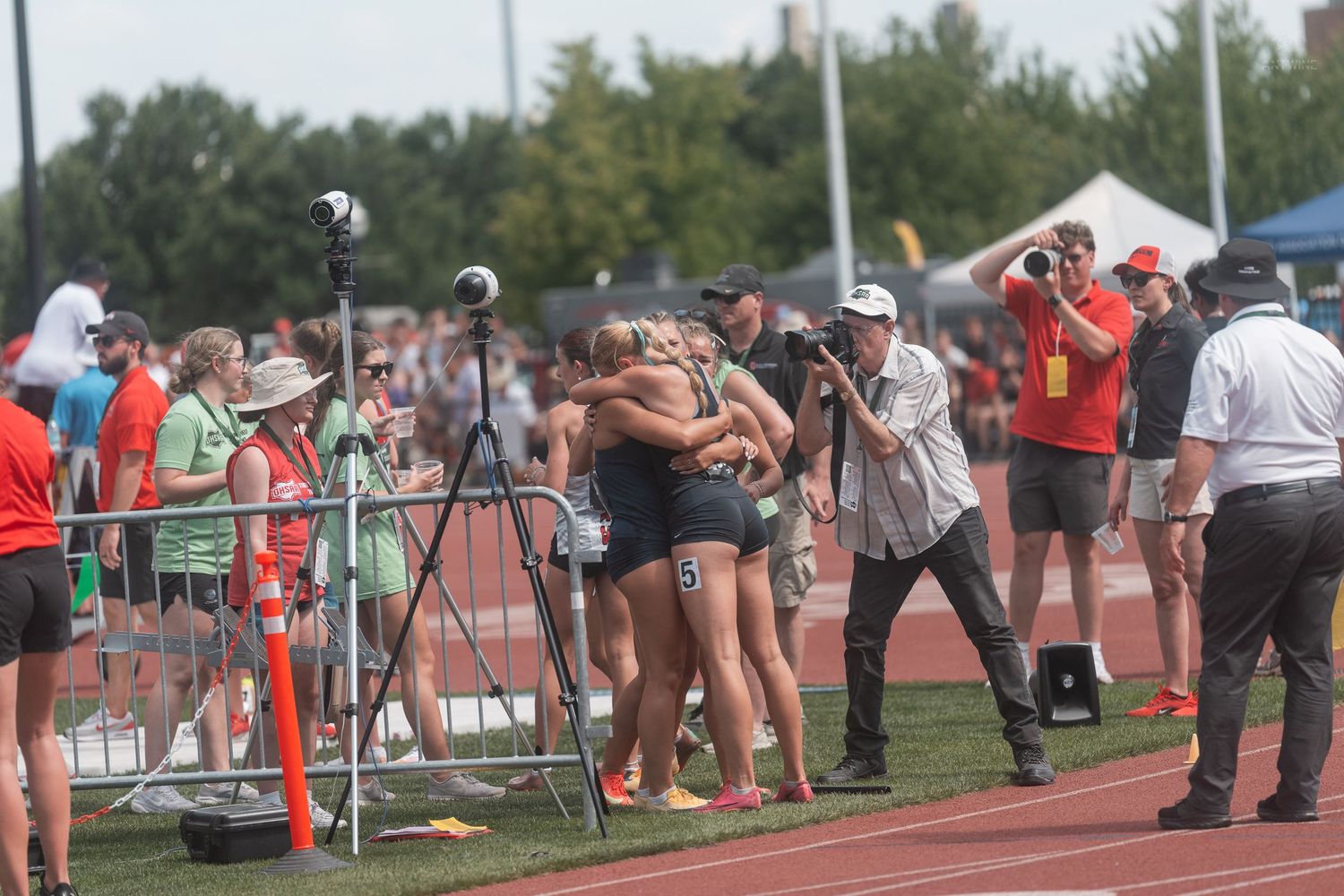 Girls track team hugging in celebration while a photographer documents the moment at a meet.