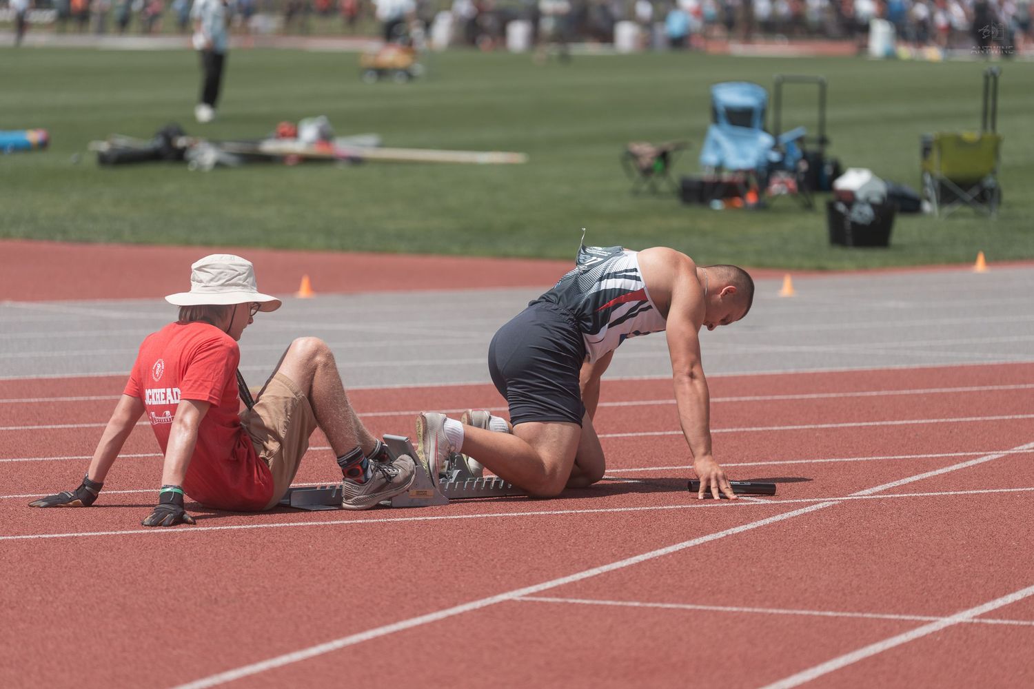 Track and field athlete in starting position assisted by official at Jesse Owens Memorial Stadium.