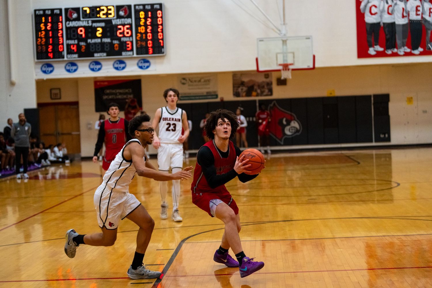 Basketball player in red drives to basket past defender in indoor gym.