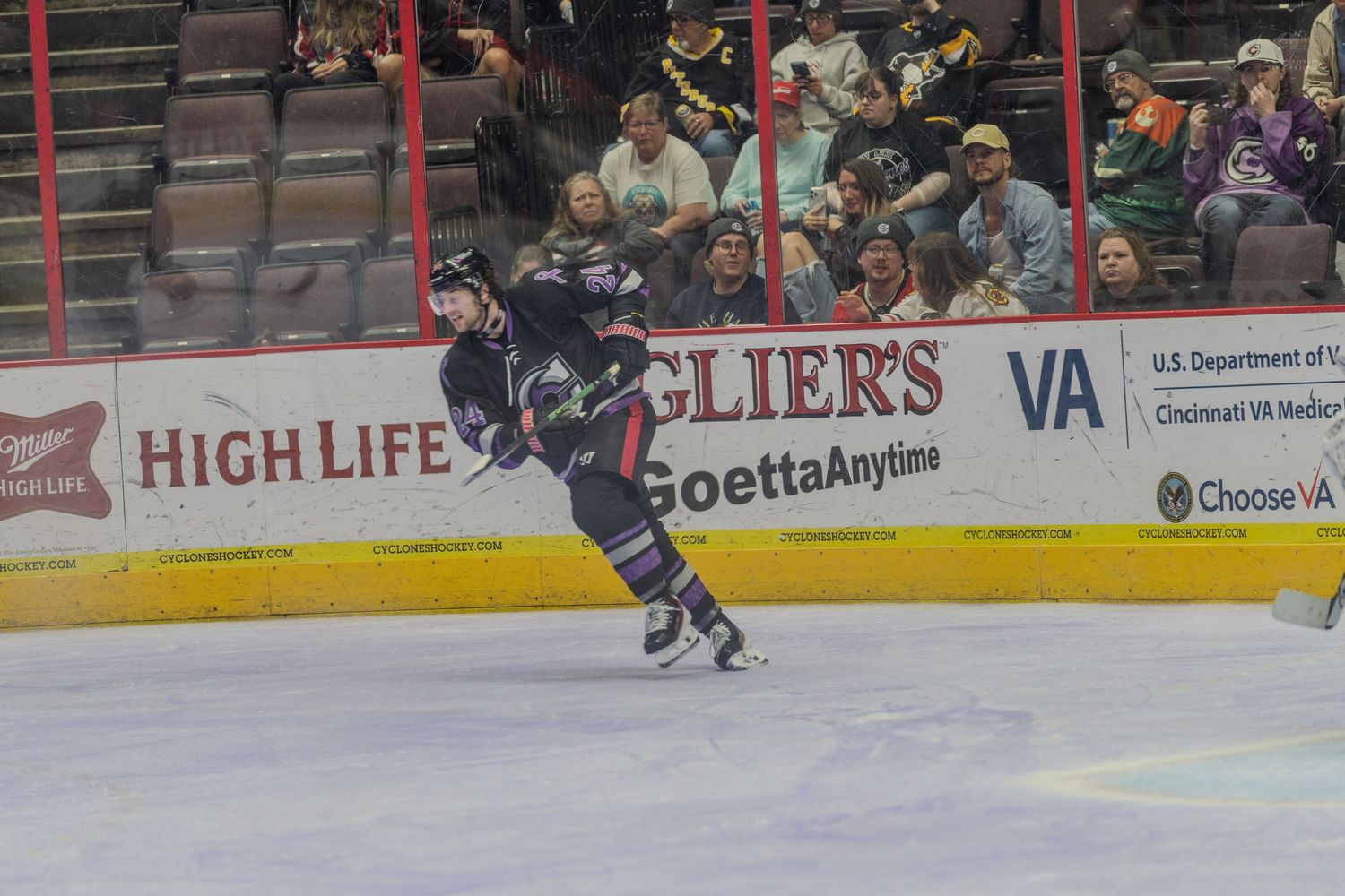 Hockey player in dark blue uniform winds up for slap shot in front of arena advertisements during game.