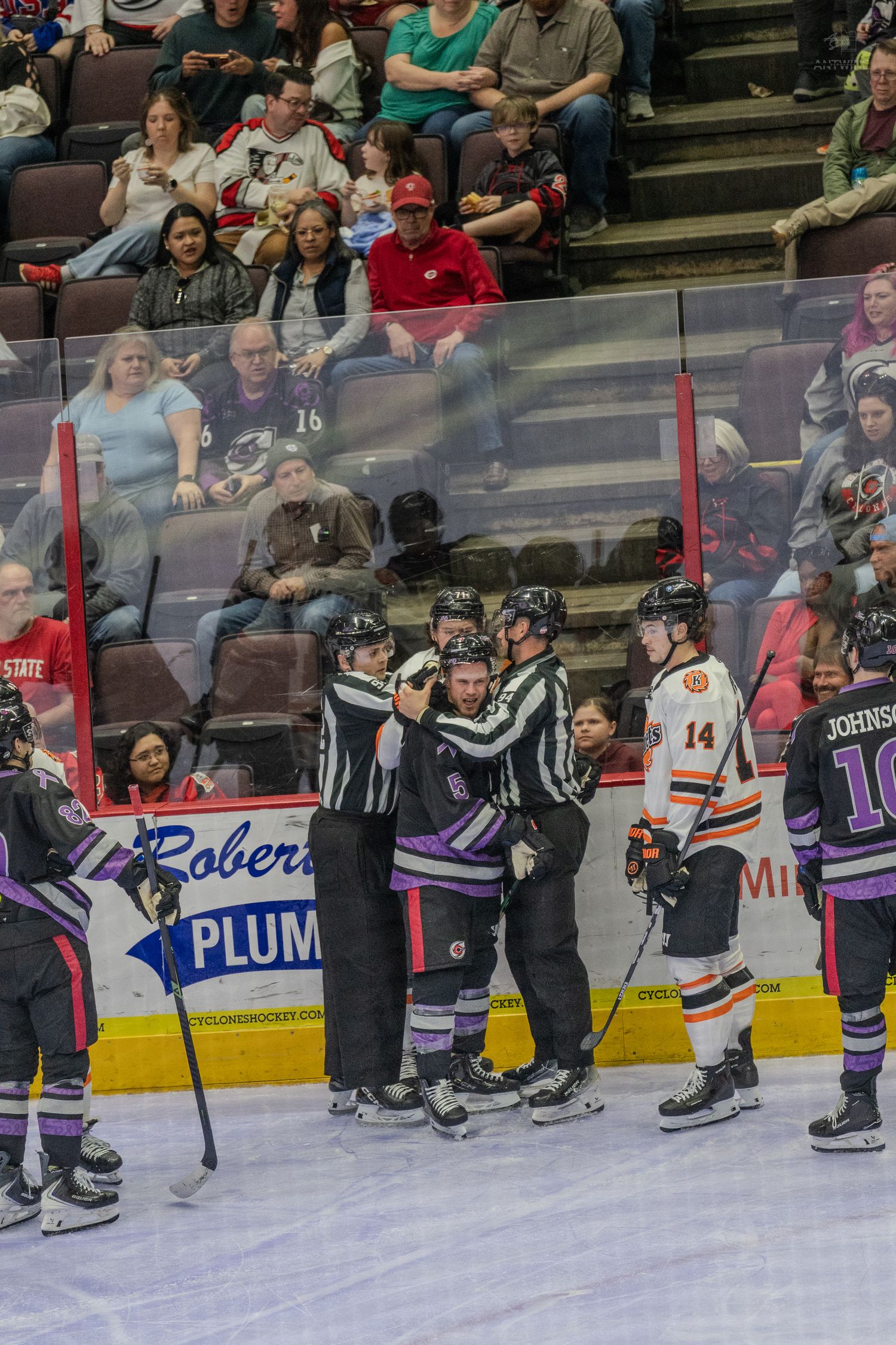 Hockey referees restrain players during a stoppage of play in a professional indoor ice hockey game.