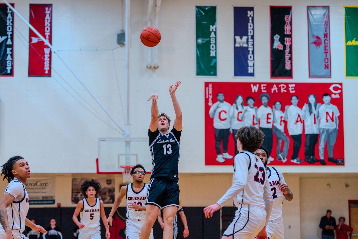 High school basketball player #13 shoots a jump shot over defenders during a game at Colerain gymnasium.