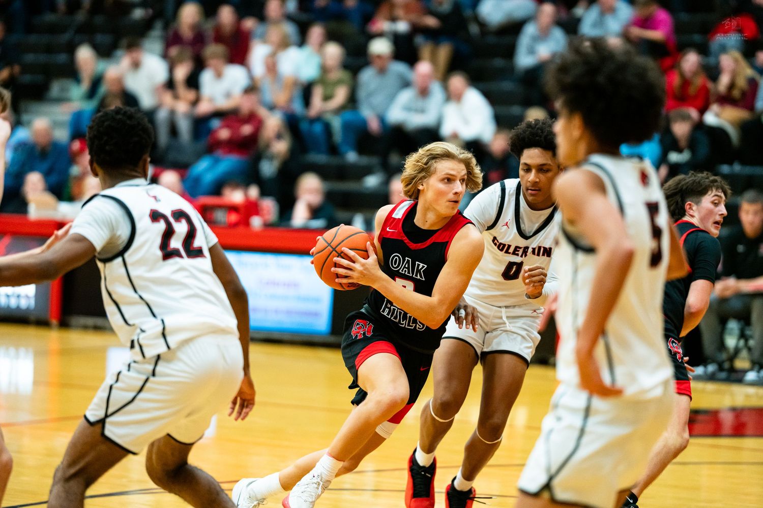 A basketball player in red drives through defenders during a competitive high school basketball game.