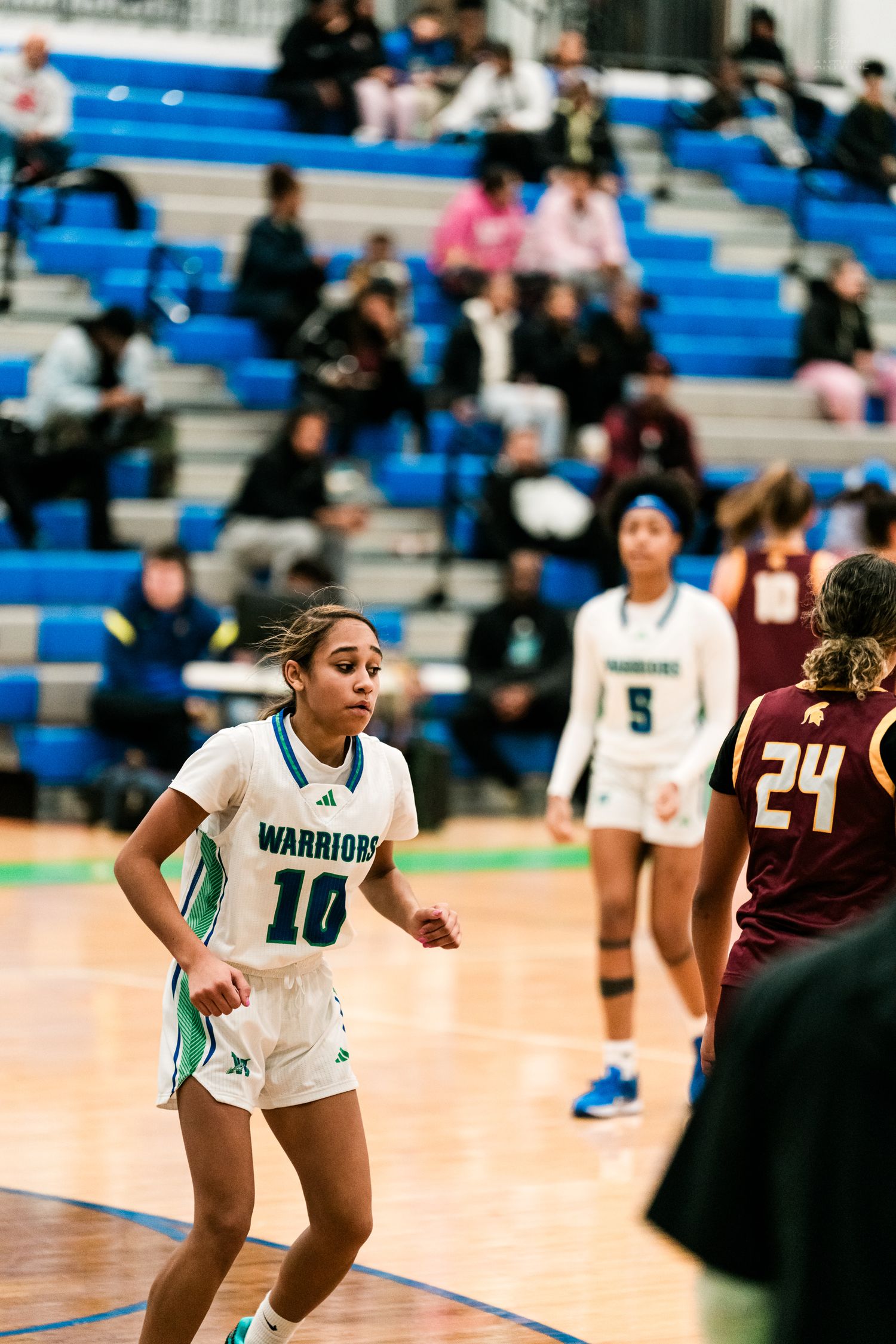 Warriors #10 guards opponent #24 in maroon uniform during girls high school basketball game in blue gymnasium.