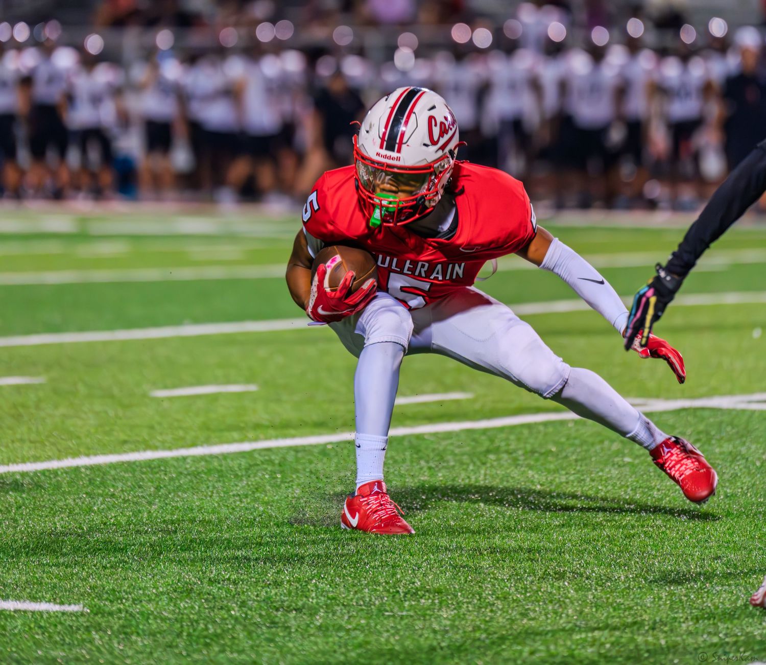 Colerain football player in red uniform makes a sharp cut while carrying the ball during a game.