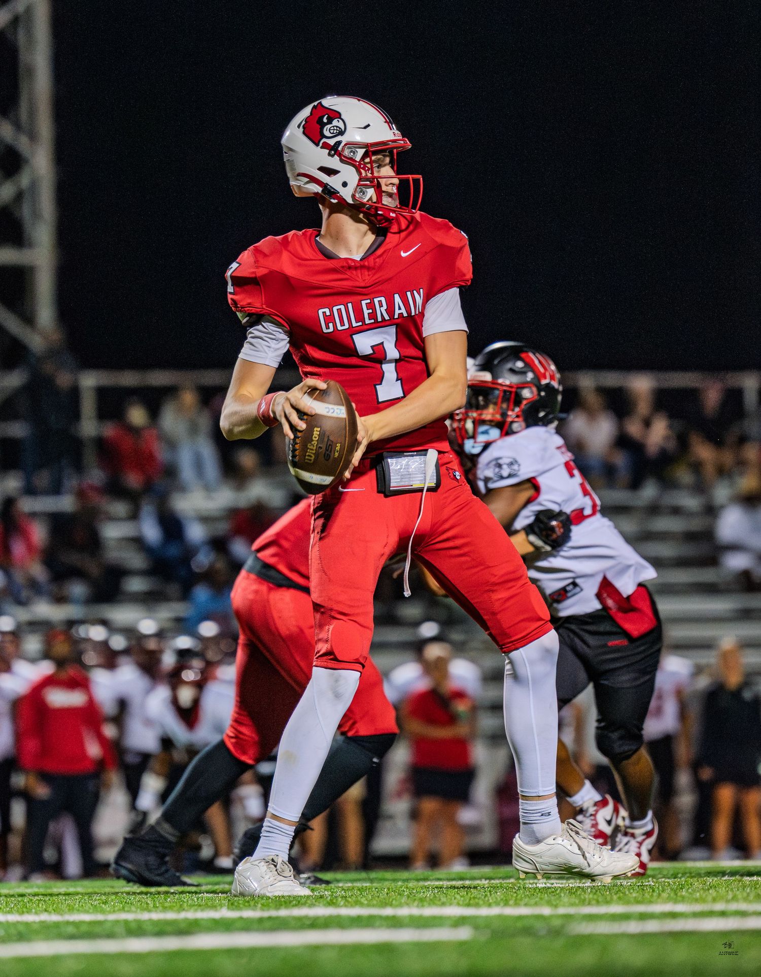 Colerain Cardinals quarterback #7 drops back to pass during a night football game.