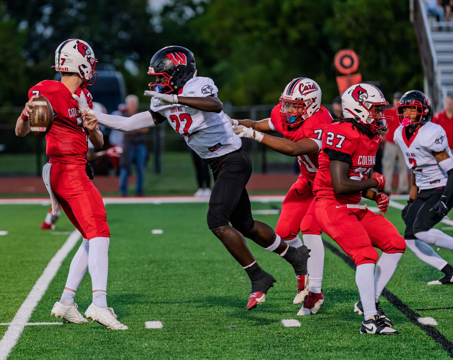 Colerain high school quarterback in red jersey releases a pass while offensive linemen block defenders.