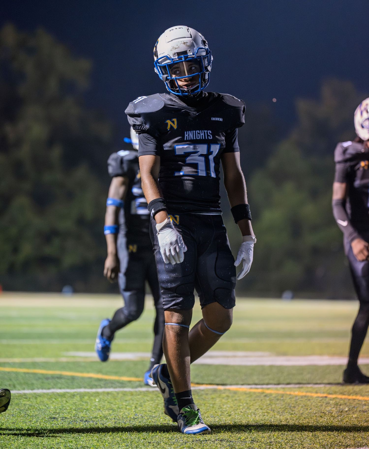 High school football player wearing black Knights jersey number 31 smiles while walking on the field.